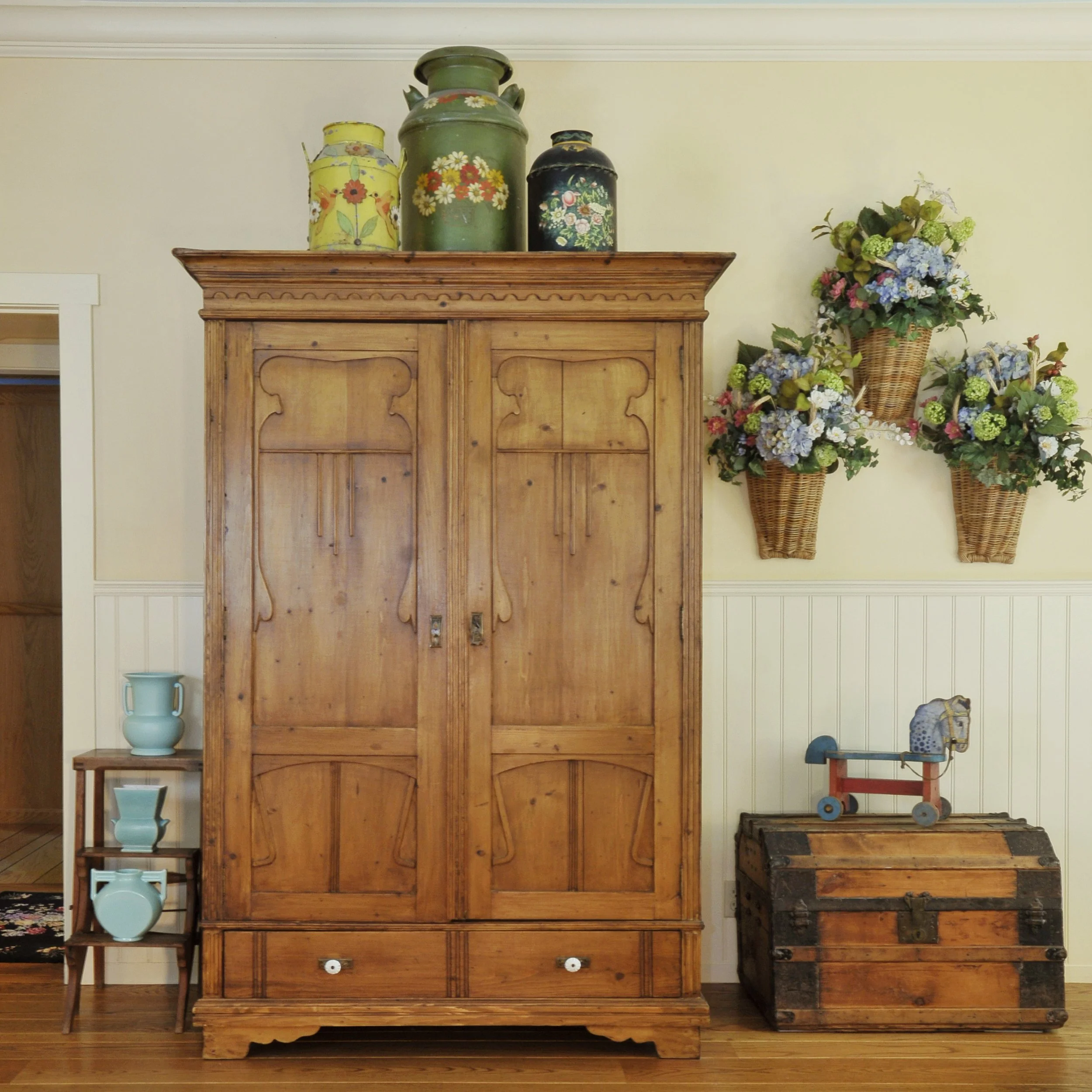 A wooden cabinet with decorative items on top, including three painted metal containers and a bouquet of flowers in baskets and vases.