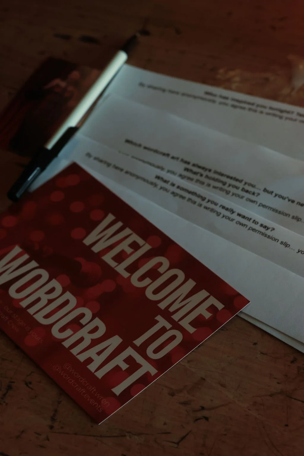 A welcome to the world card and a document on a wooden table, with a pen placed on top of the document.