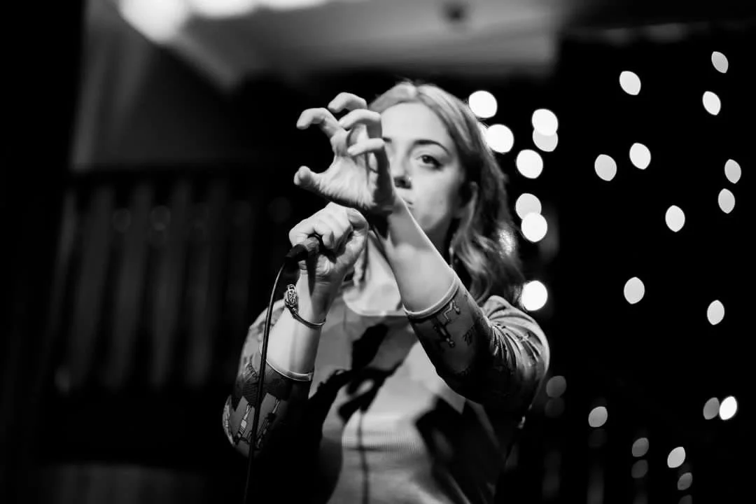 A woman holding a microphone and gesturing with her hand during a performance.