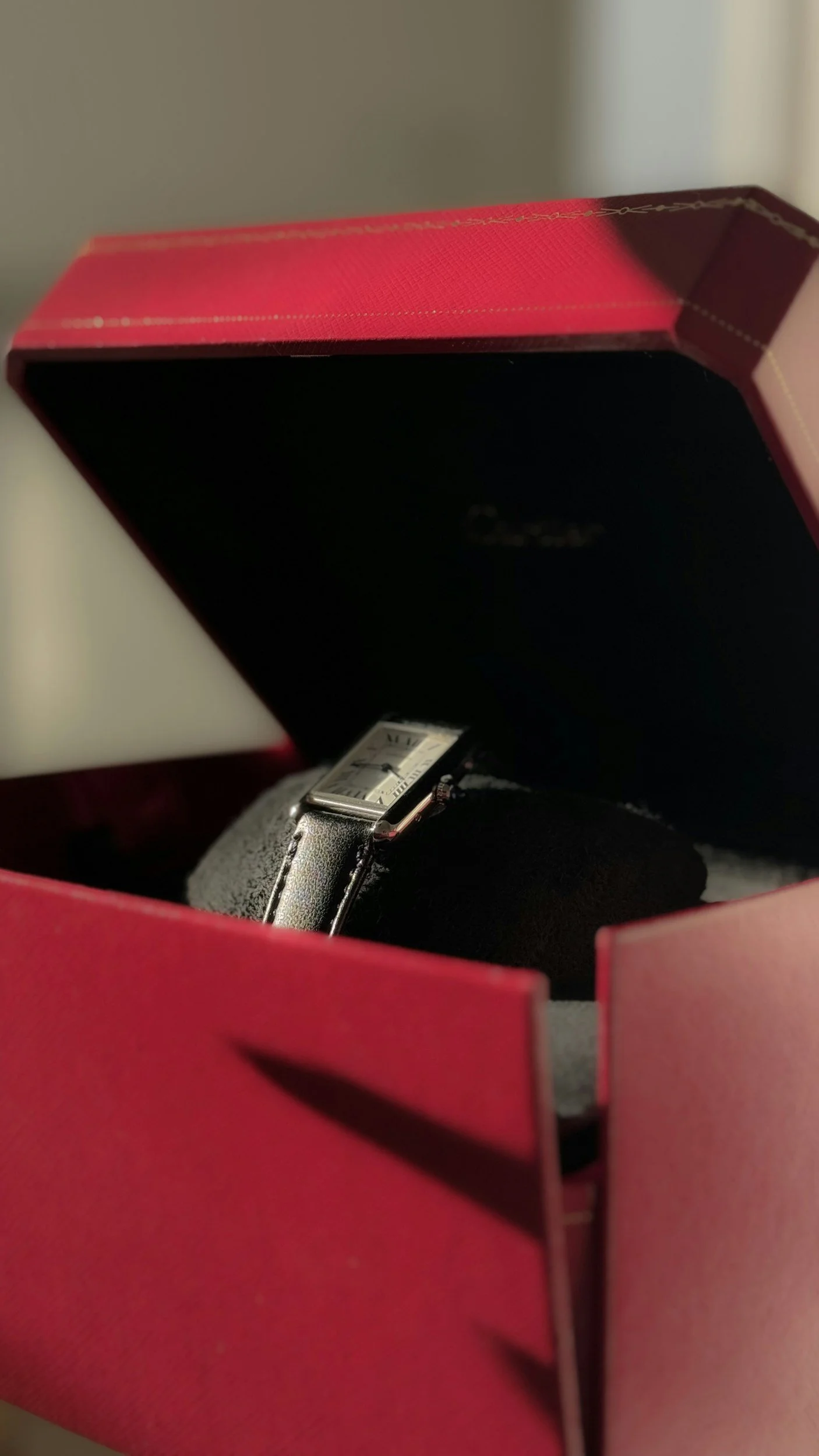 A wristwatch with a silver rectangular face and black leather strap inside a pink box.