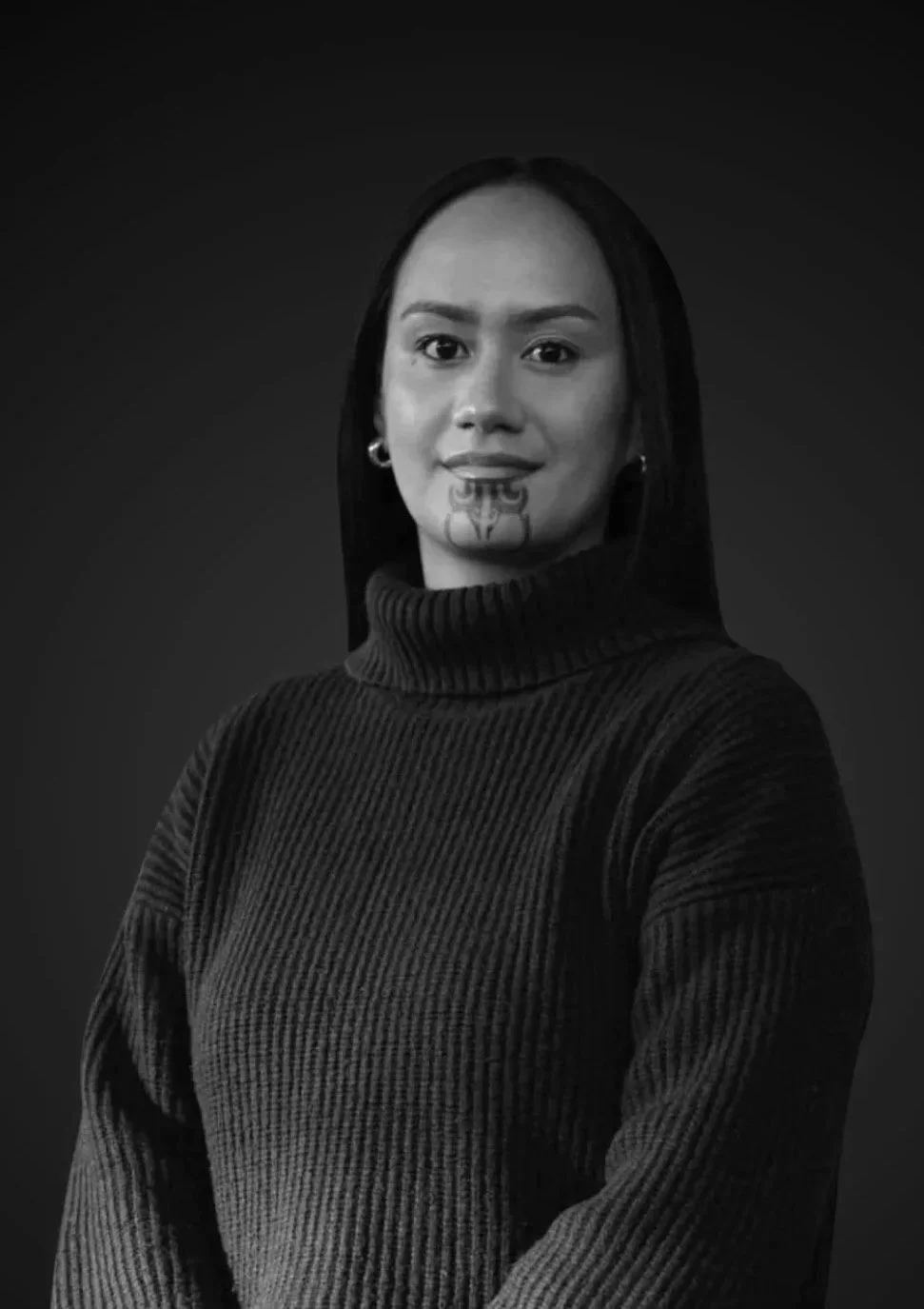 Portrait of a young woman with long dark hair, smiling, wearing a button-up shirt, against a dark background.