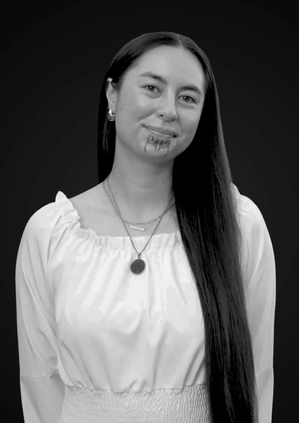Black and white portrait of a smiling woman wearing a light-colored sweater, jewelry, and earrings, against a dark background.
