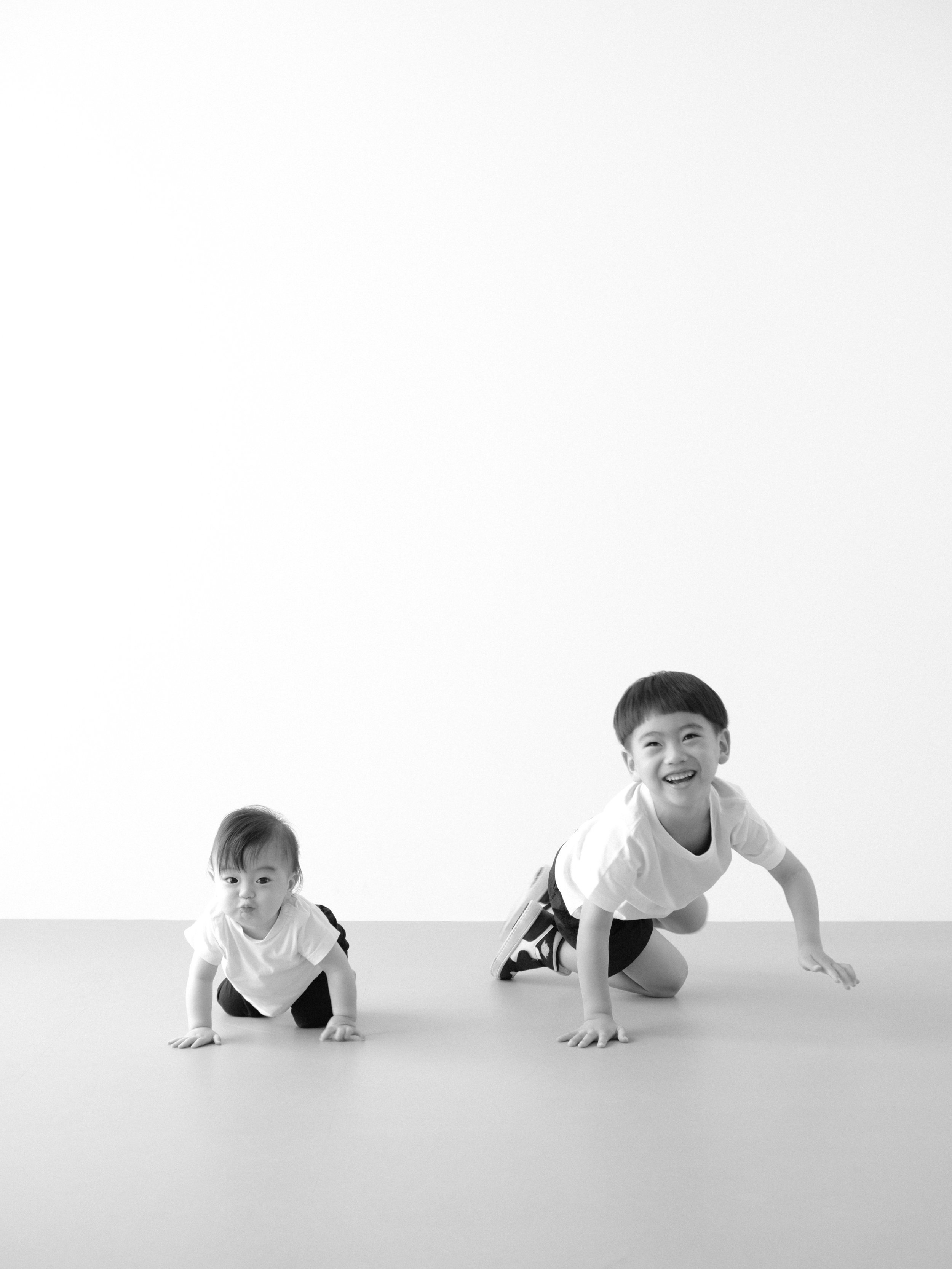 白い背景の上に2人の子供がハイハイのポーズをしている。兄弟写真。