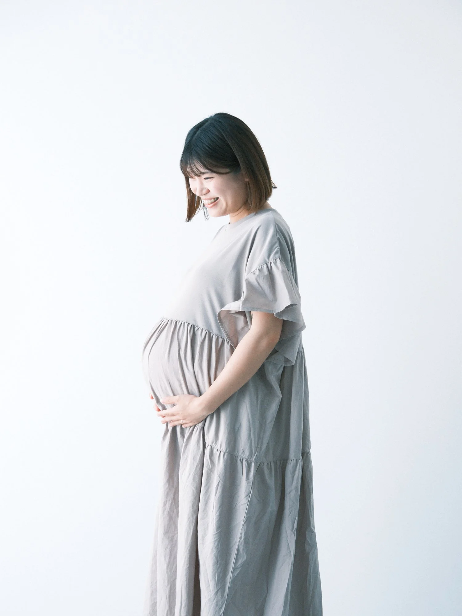 妊娠している女性が優しくお腹をさする姿。白い背景の前でシンプルに撮影した写真。