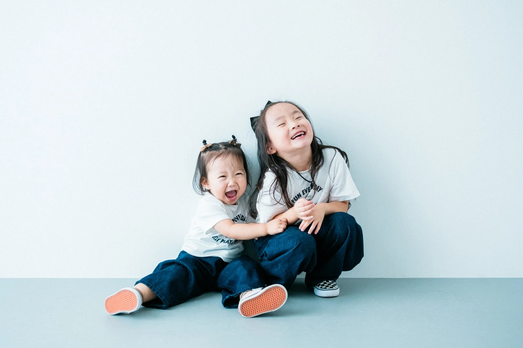 笑顔の二人の女の子が壁に寄りかかって座っている、姉妹の写真。