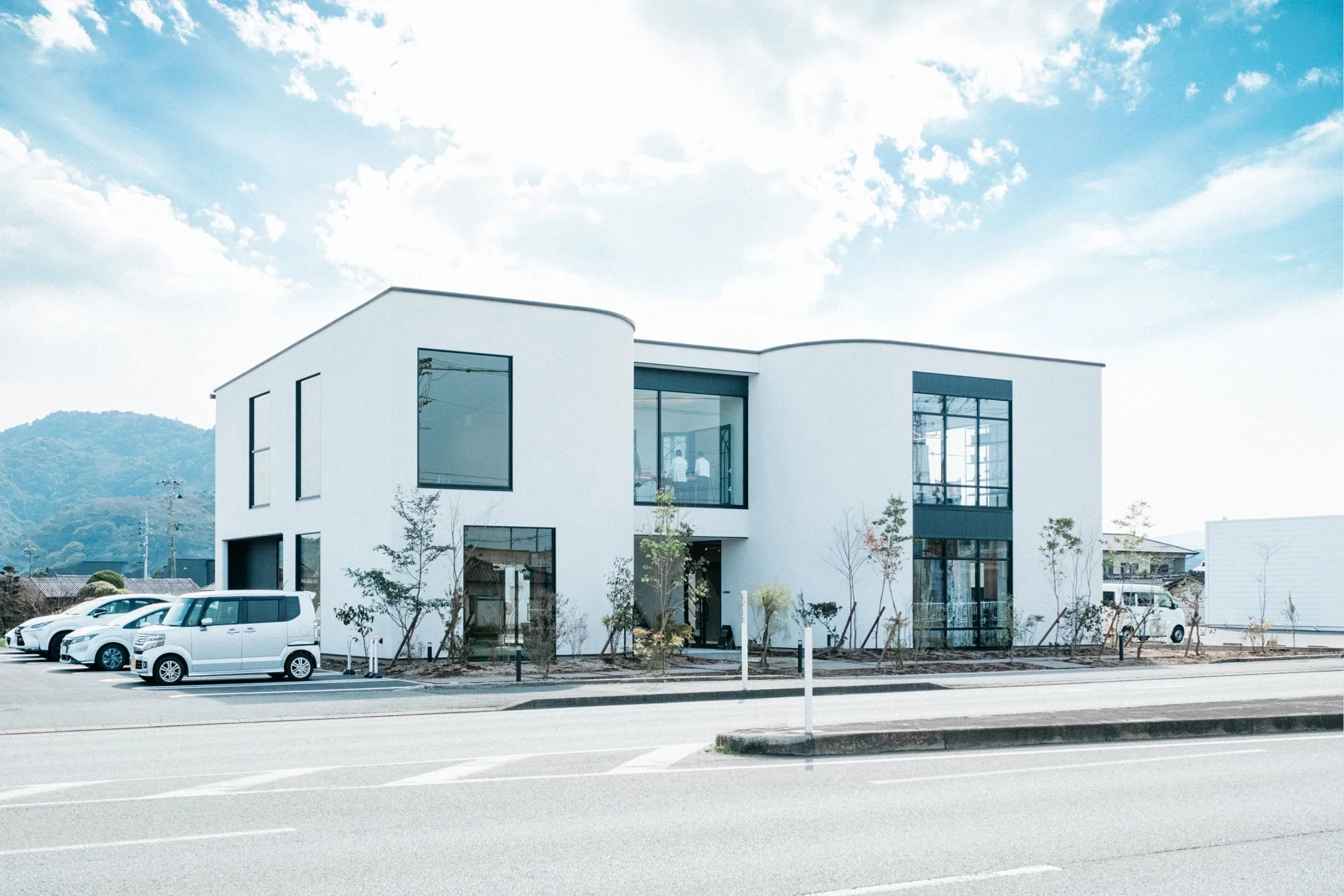熊本市南区富合町にある白い現代的な商業的建物、青空と雲、遠くに山が見える風景。