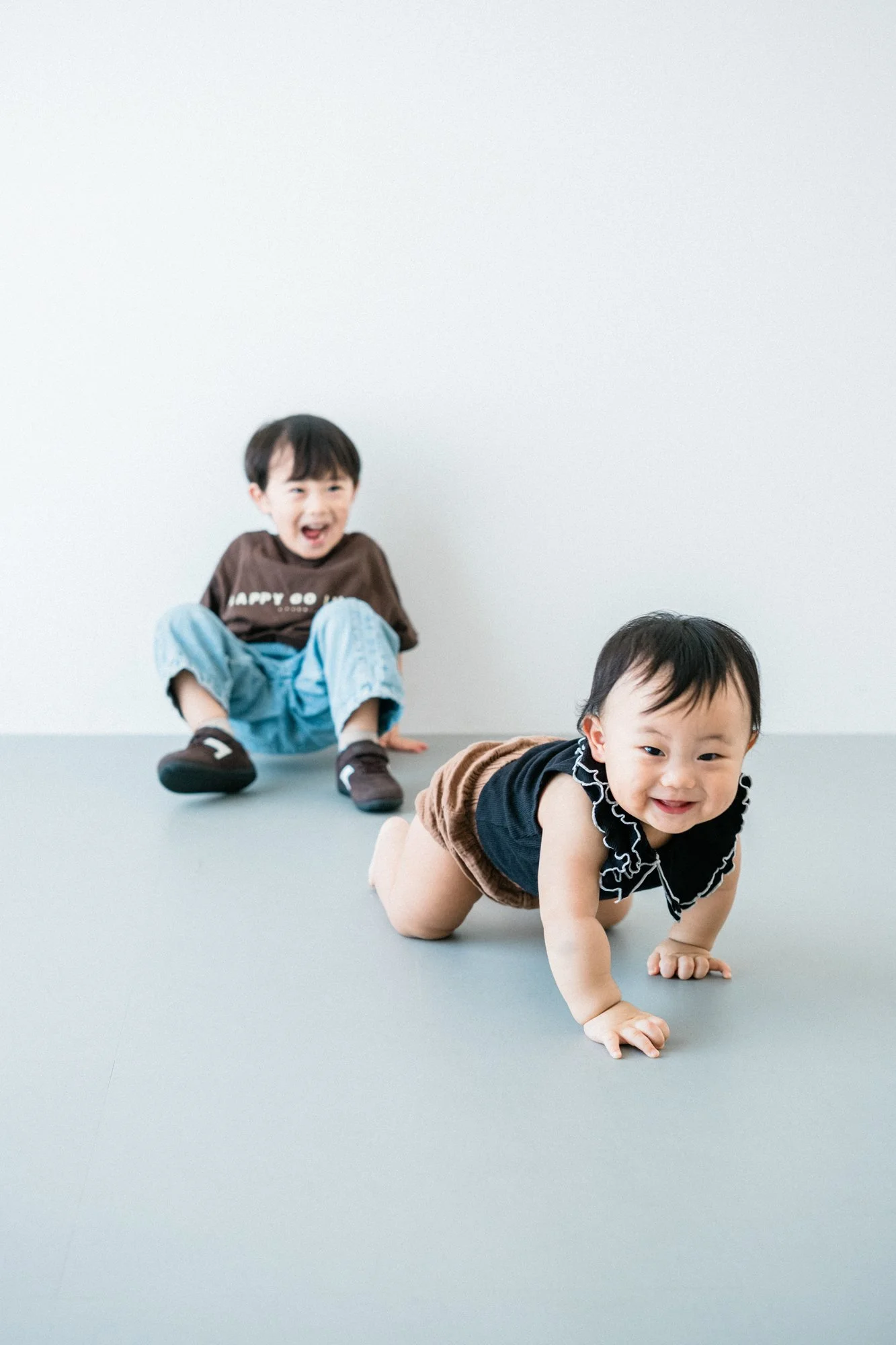 床の上で遊ぶ二人の幼い子供、ハイハイで笑顔でポーズをとる