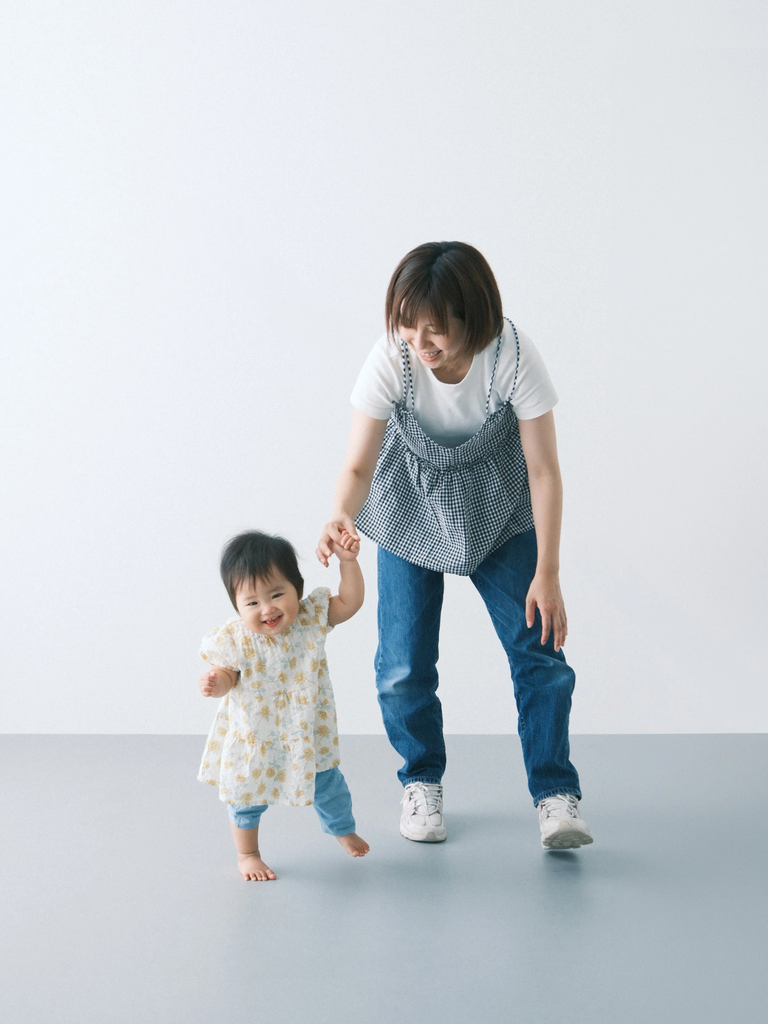 お母さんと女の子が白い背景の前で手をつないで歩いているセルフフォトの写真。