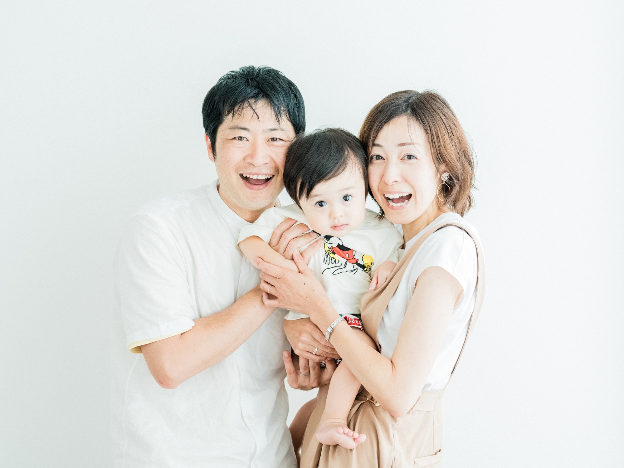 白い背景の前で笑顔の家族が抱き合っている写真。ナチュラルな家族写真。