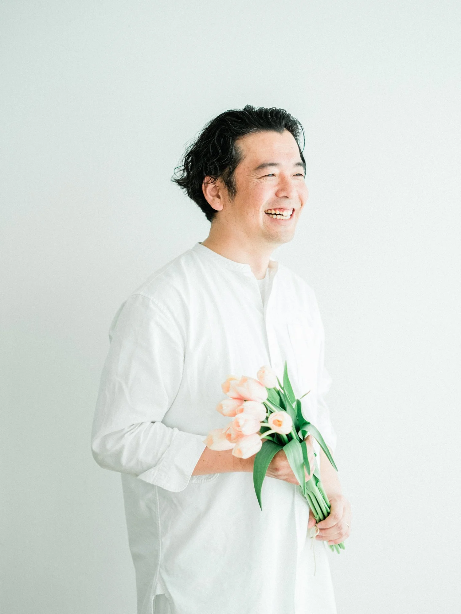 白いシャツを着たオーナーがピンクのチューリップの花束を持ち、笑顔でいる写真。
