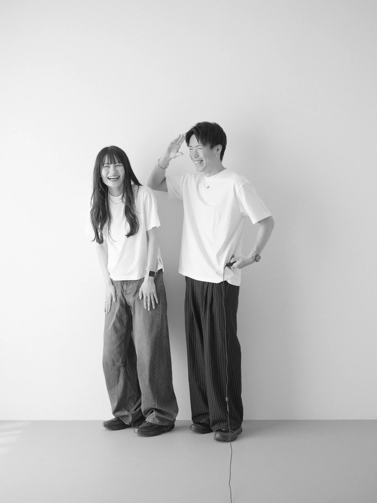 白い背景の前で笑顔の楽しそうなカップルが白Tシャツを着ている。モノクロのセルフフォト。