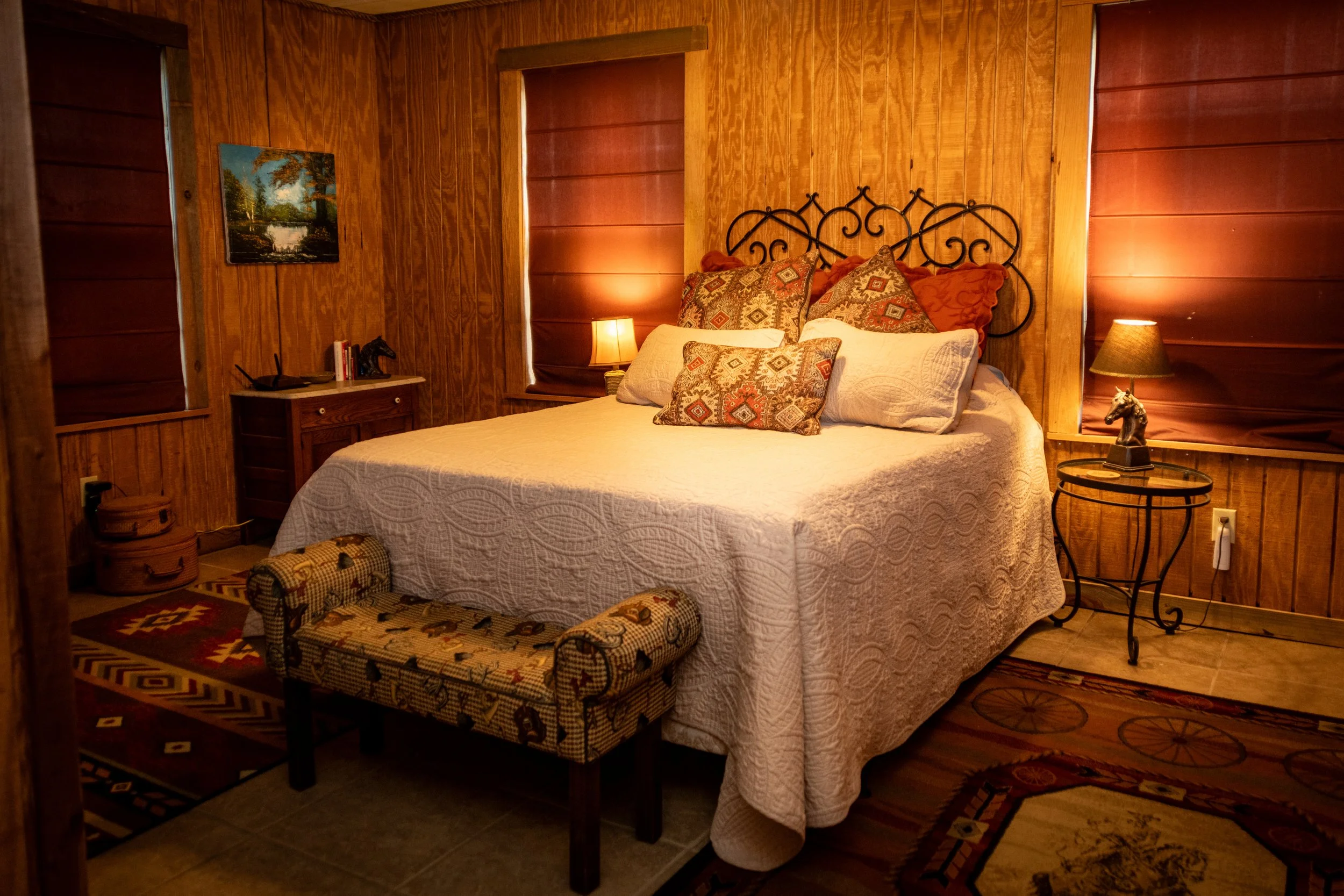 Cozy bedroom with wood-paneled walls, a wrought iron bed frame, patterned pillows, and warm lighting from lamps on bedside tables.