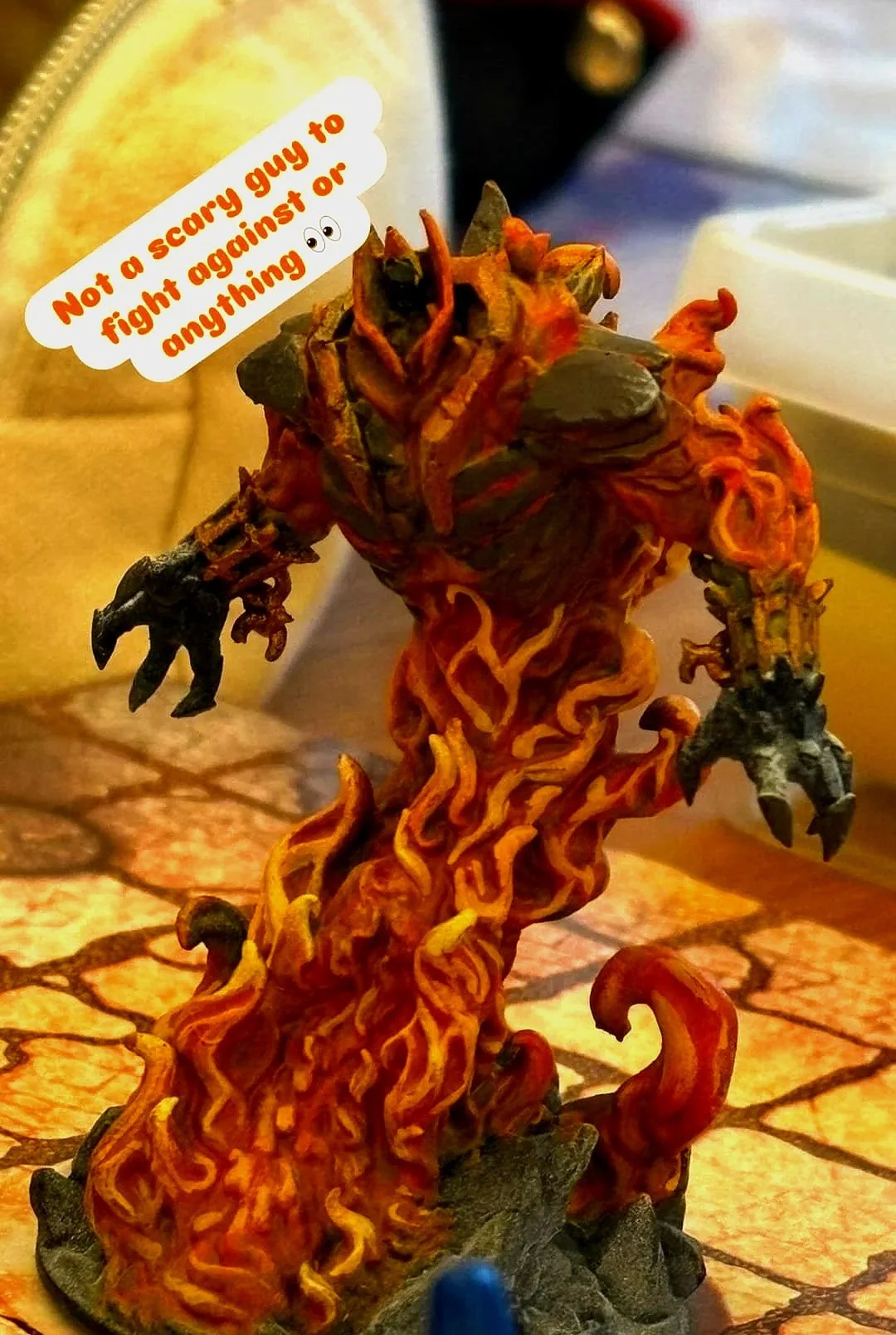 A detailed figure of a monstrous creature with fiery, twisted body, large sharp claws, and a menacing stance. It has a speech bubble saying, 'Not a scary guy to fight against or anything 😊.'