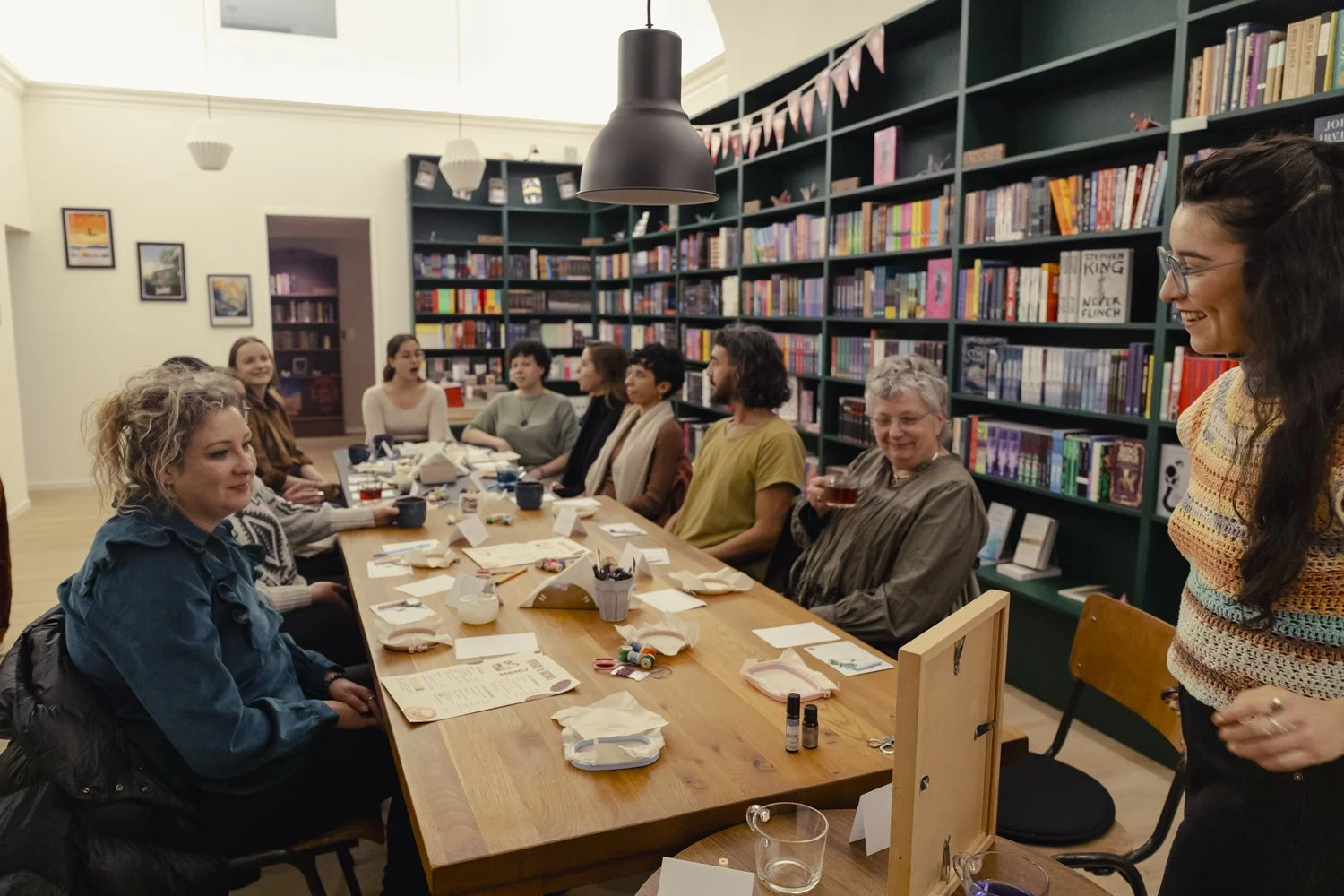 A group of women sitting around a wooden table in a cozy library, engaging in a book club or meeting, with bookshelves full of colorful books in the background.