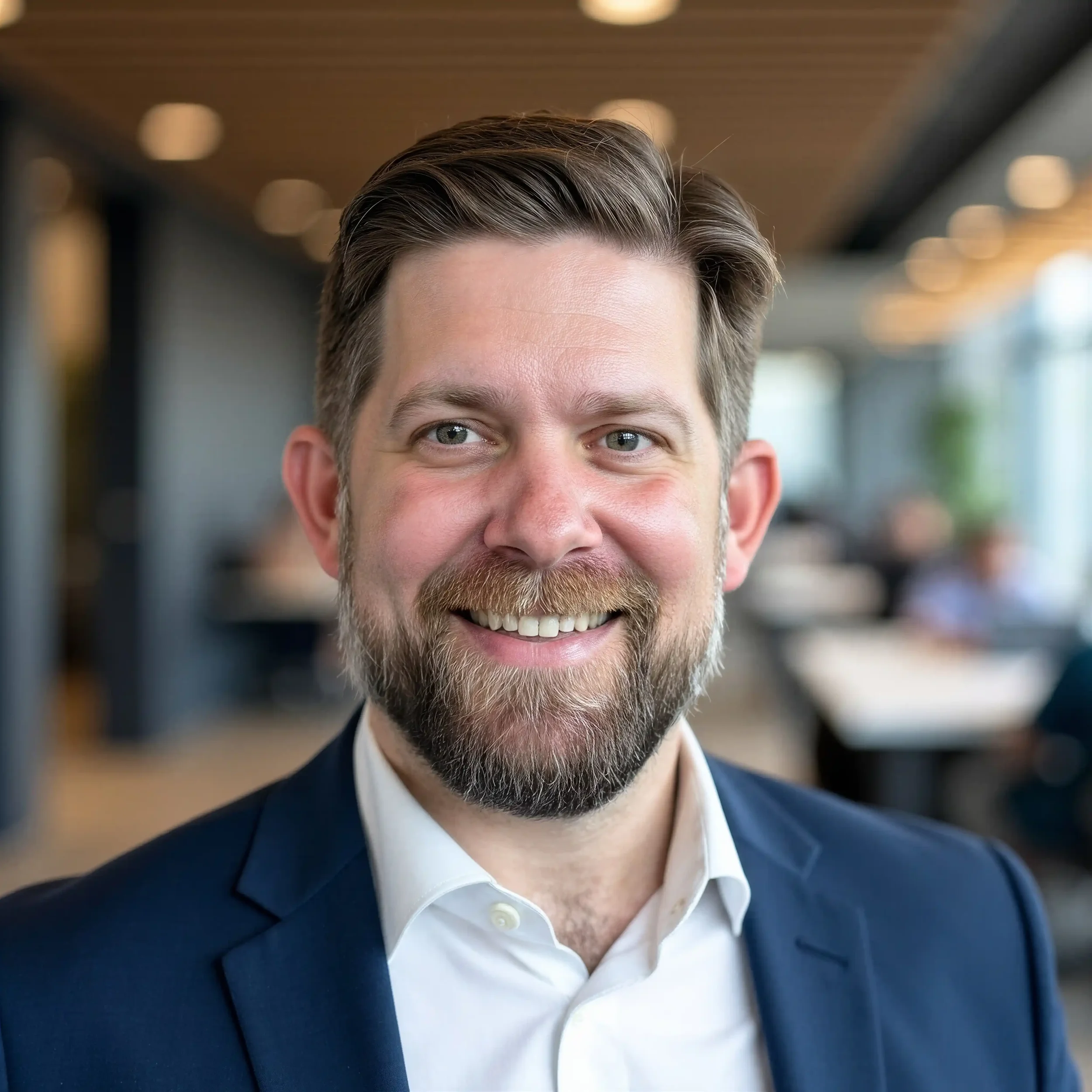 Close-up of a Andy smiling with gray hair and beard, wearing a white shirt and dark blazer.