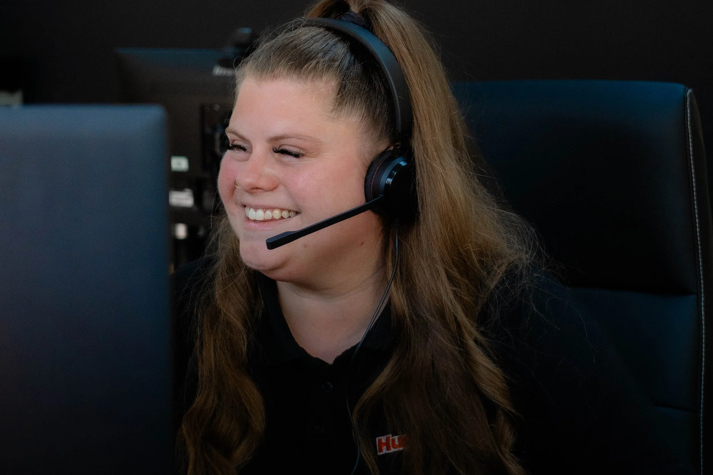 Smiling woman with long brown hair wearing headphones, sitting at a computer.