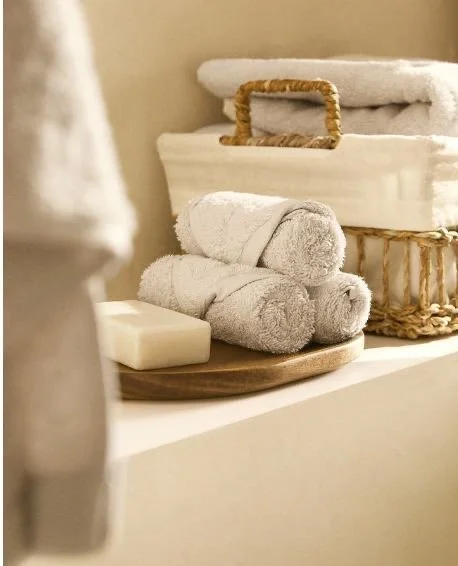 Stacked white towels, a bar of soap, and folded towels in a decorative basket on a shelf.