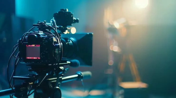 Camera on a tripod in a dimly lit studio with blurred lights in the background.