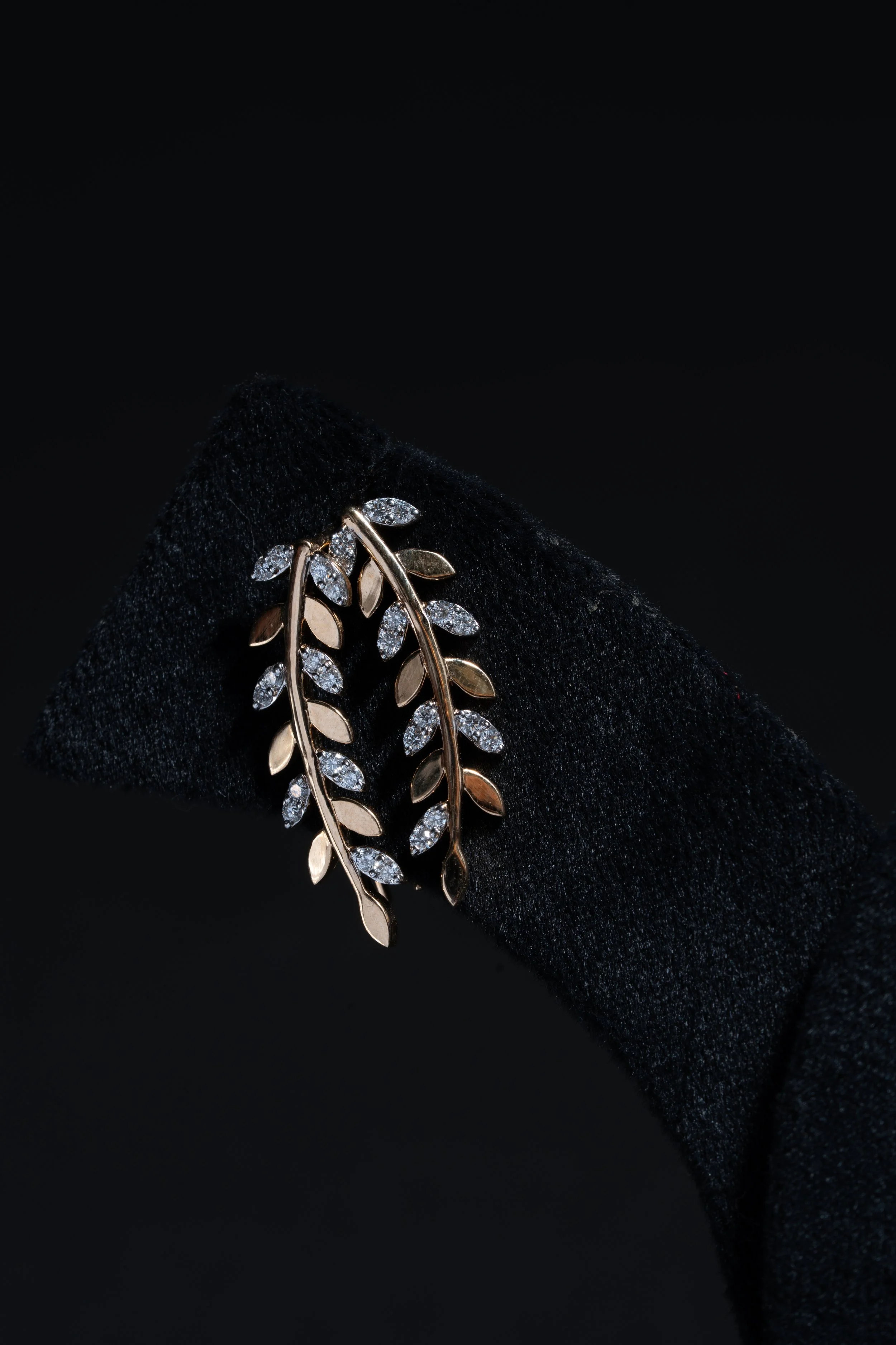 Gold leaf-shaped jewelry with embedded diamonds, displayed on a black velvet background.