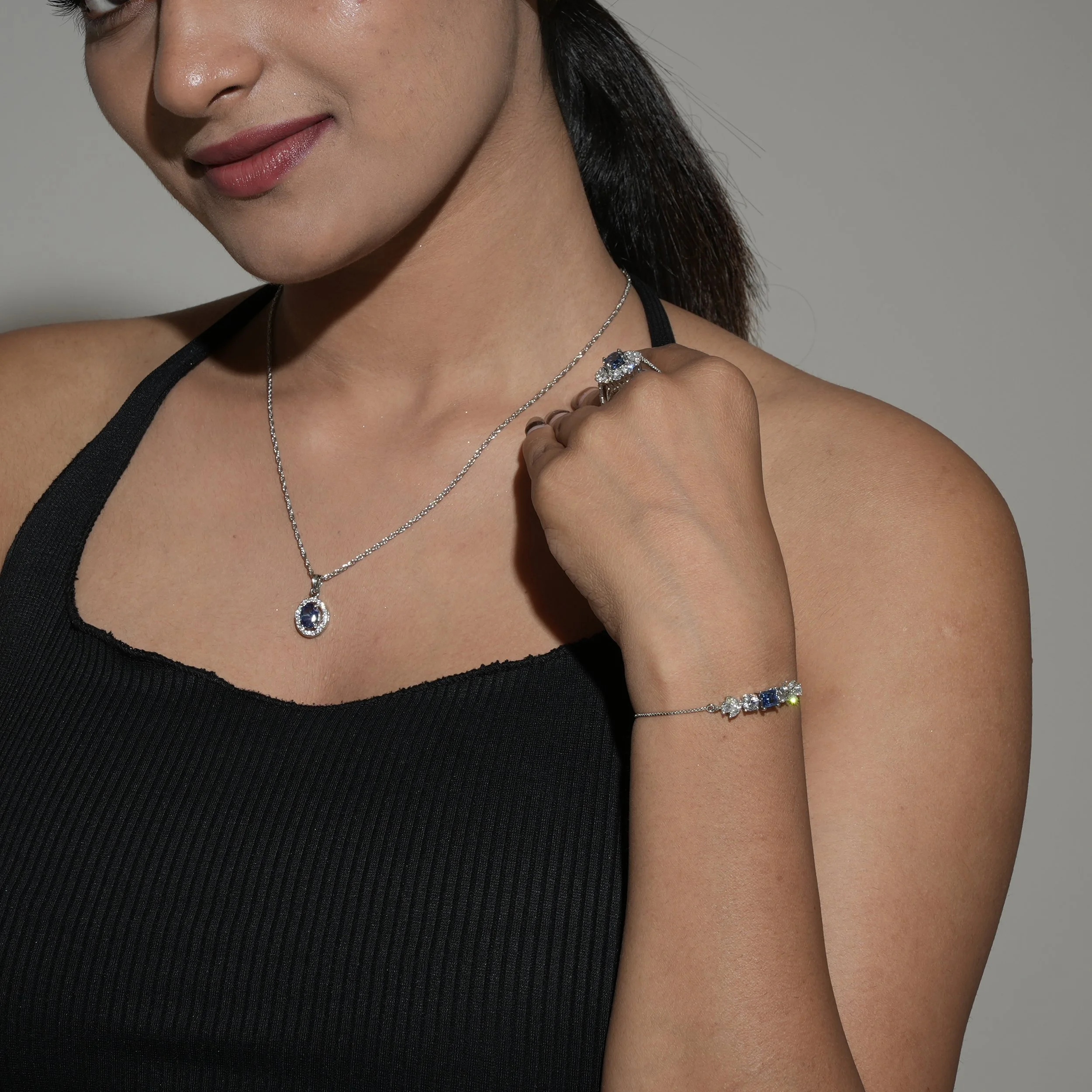 A woman wearing a black top is shown with jewelry, including a necklace, ring, bracelet, and earrings.