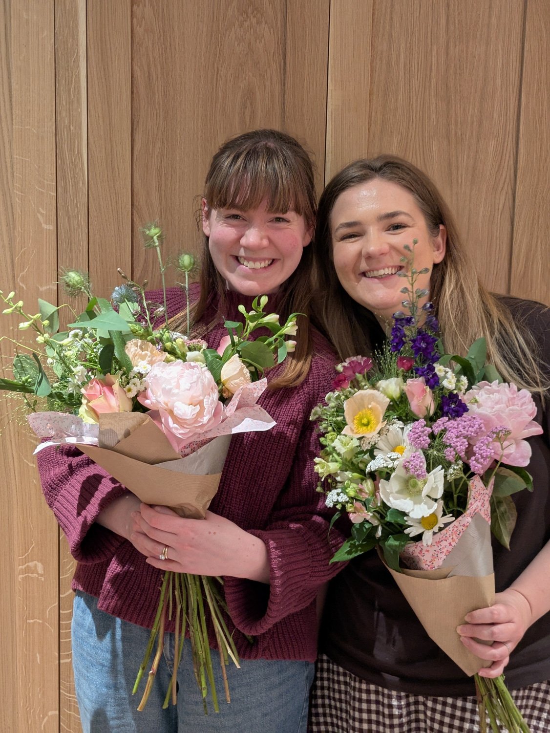 Two smilig women holding their hand made colourful workshop bouquets