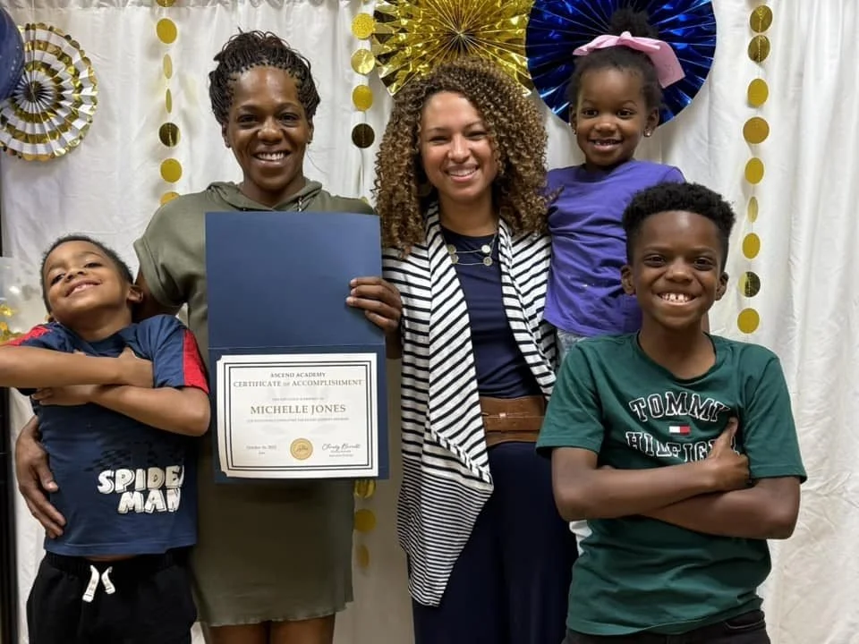 A woman holding a certificate with three children around her, celebrating an achievement at a decorated event.