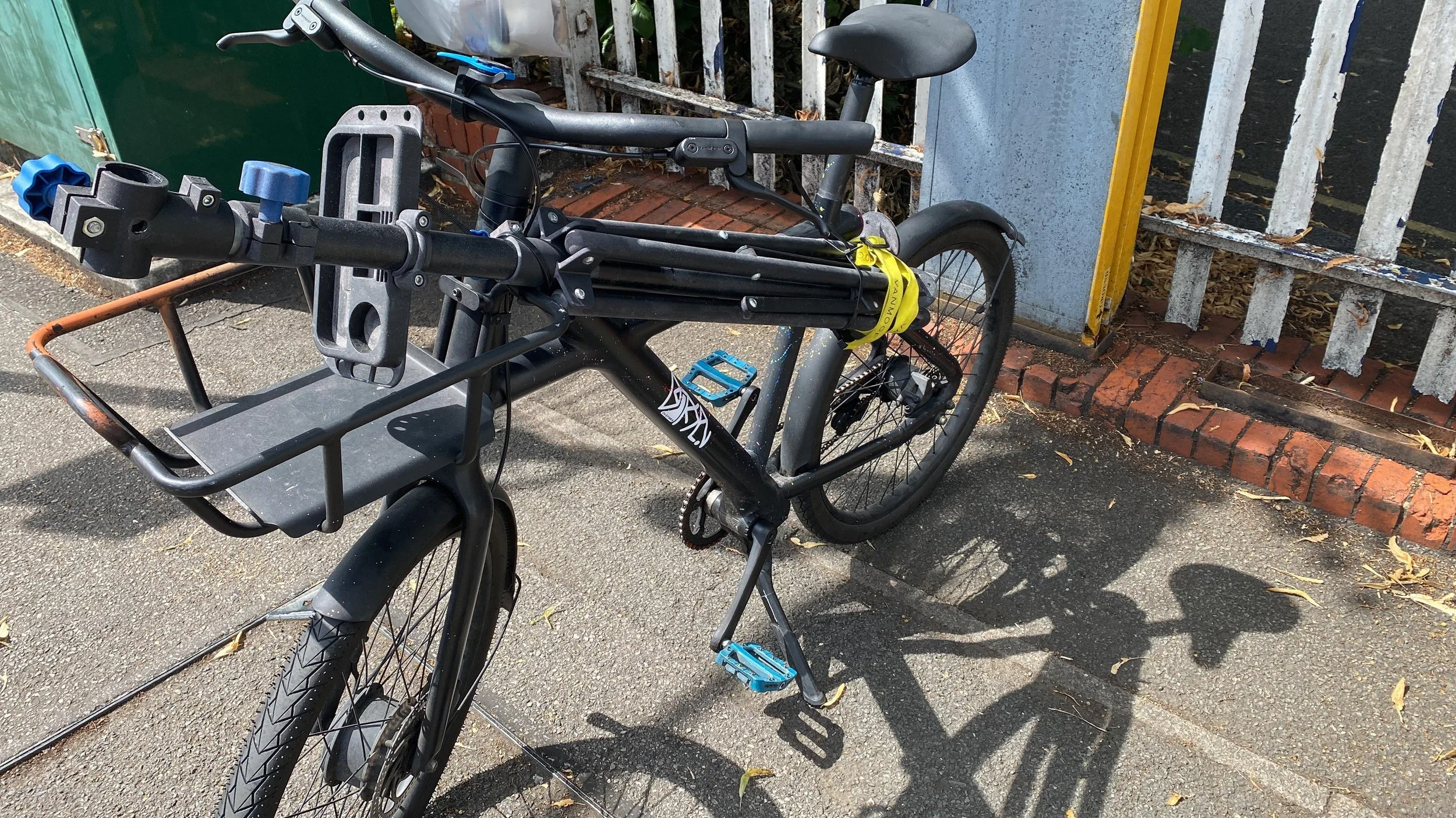 A black bicycle with a front basket parked outside near a white metal fence and brick sidewalk.