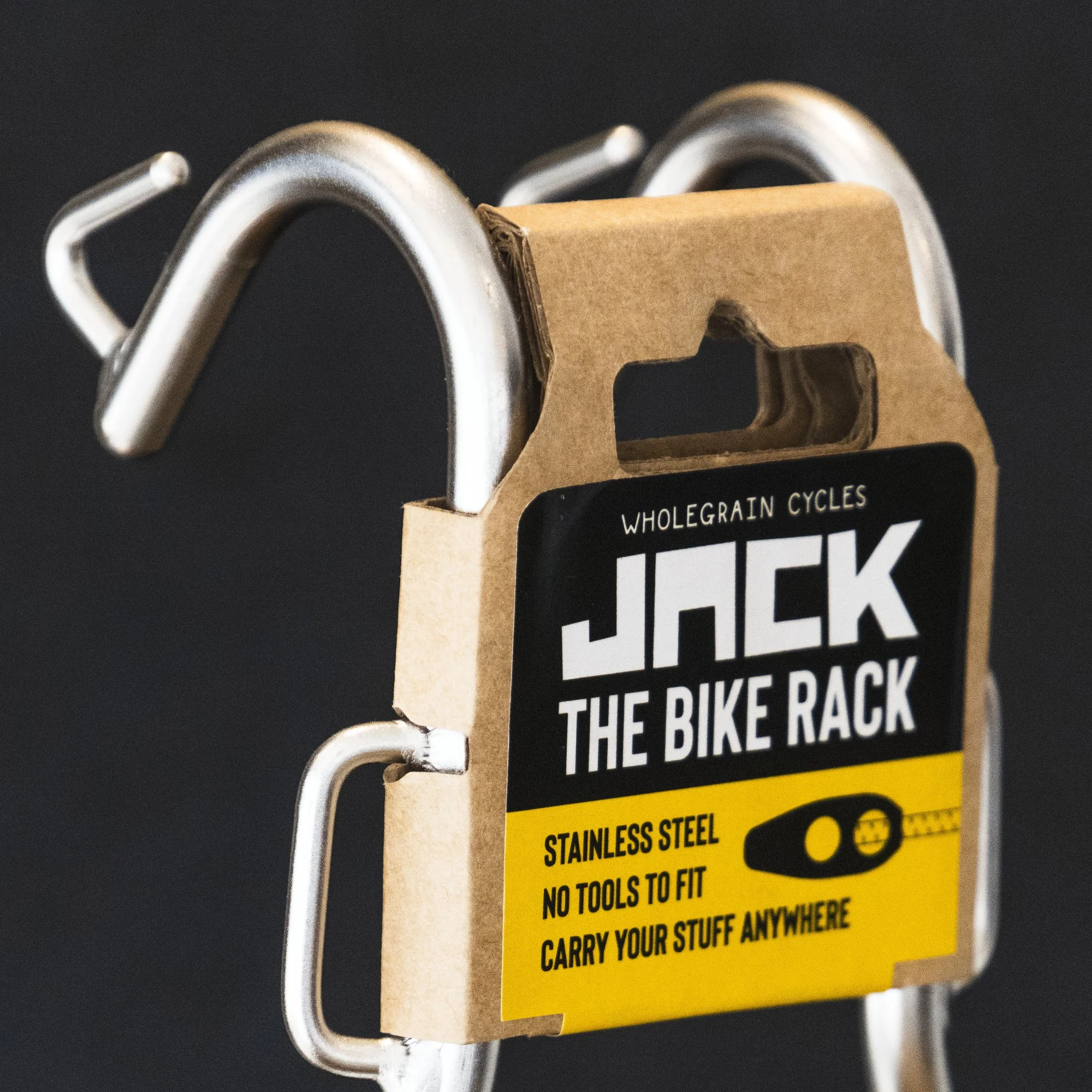 Close-up of a silver bike rack with a cardboard sign attached, displaying text about carrying tools and steel.