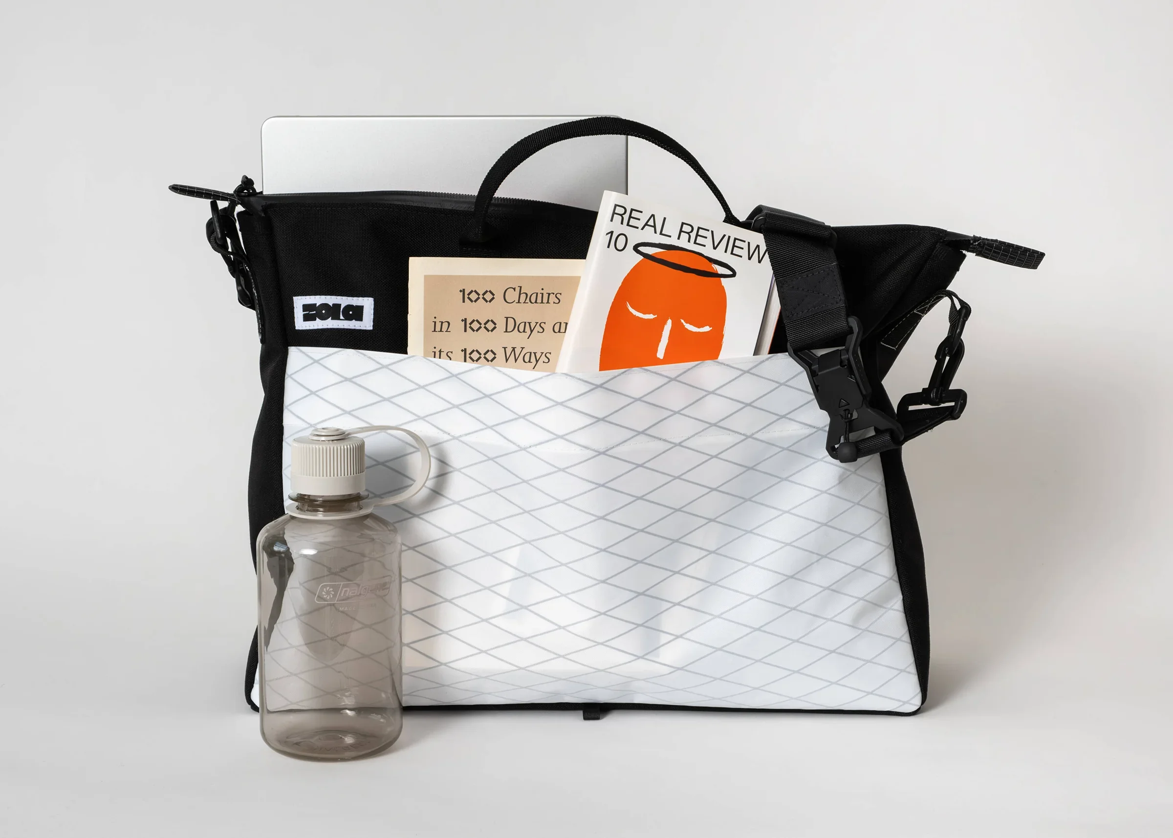 A black bag filled with various items including magazines, a water bottle, and a laptop, set against a plain white background.