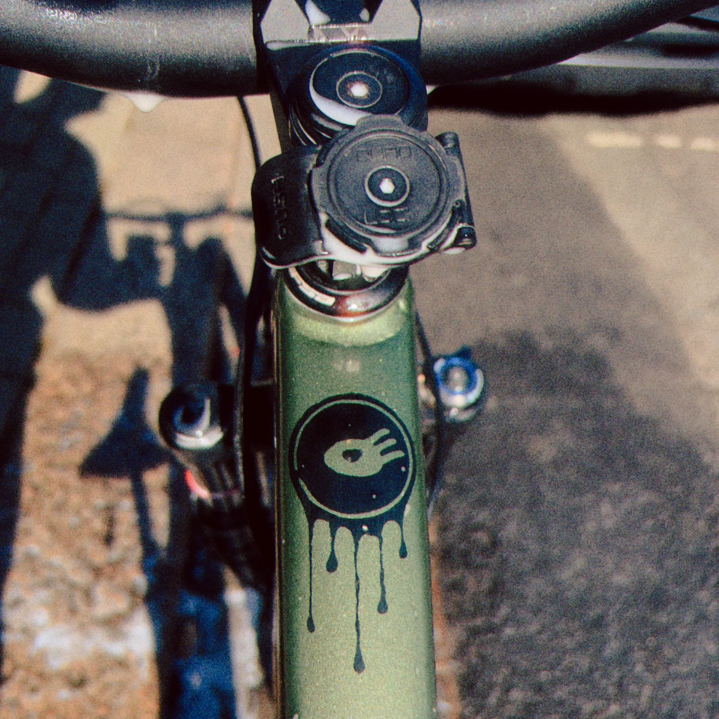 Close-up of a bicycle handlebar with a black Garmin GPS device and a digital gear shifter, with some paint drips on the frame.