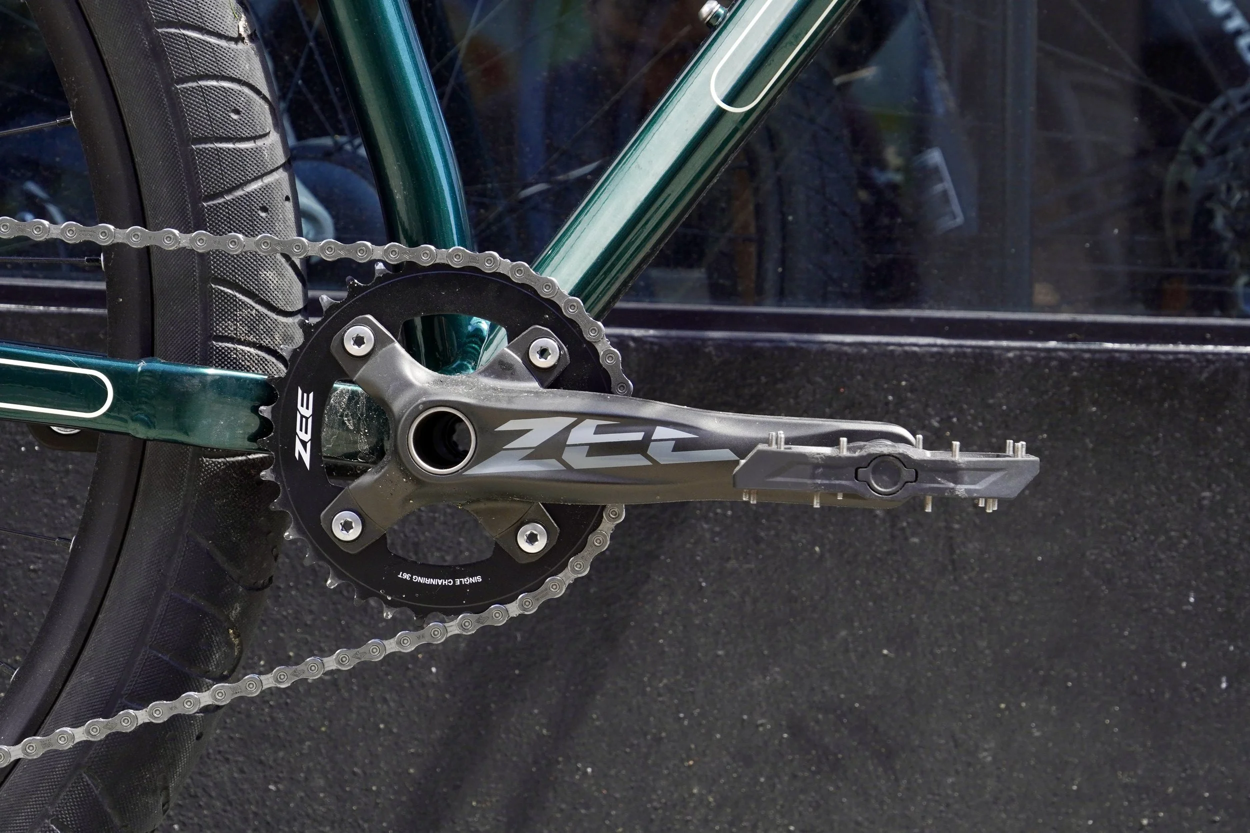 Close-up of a bicycle chainring, crankset, and rear tire, with a green frame and a transparent bike guard.