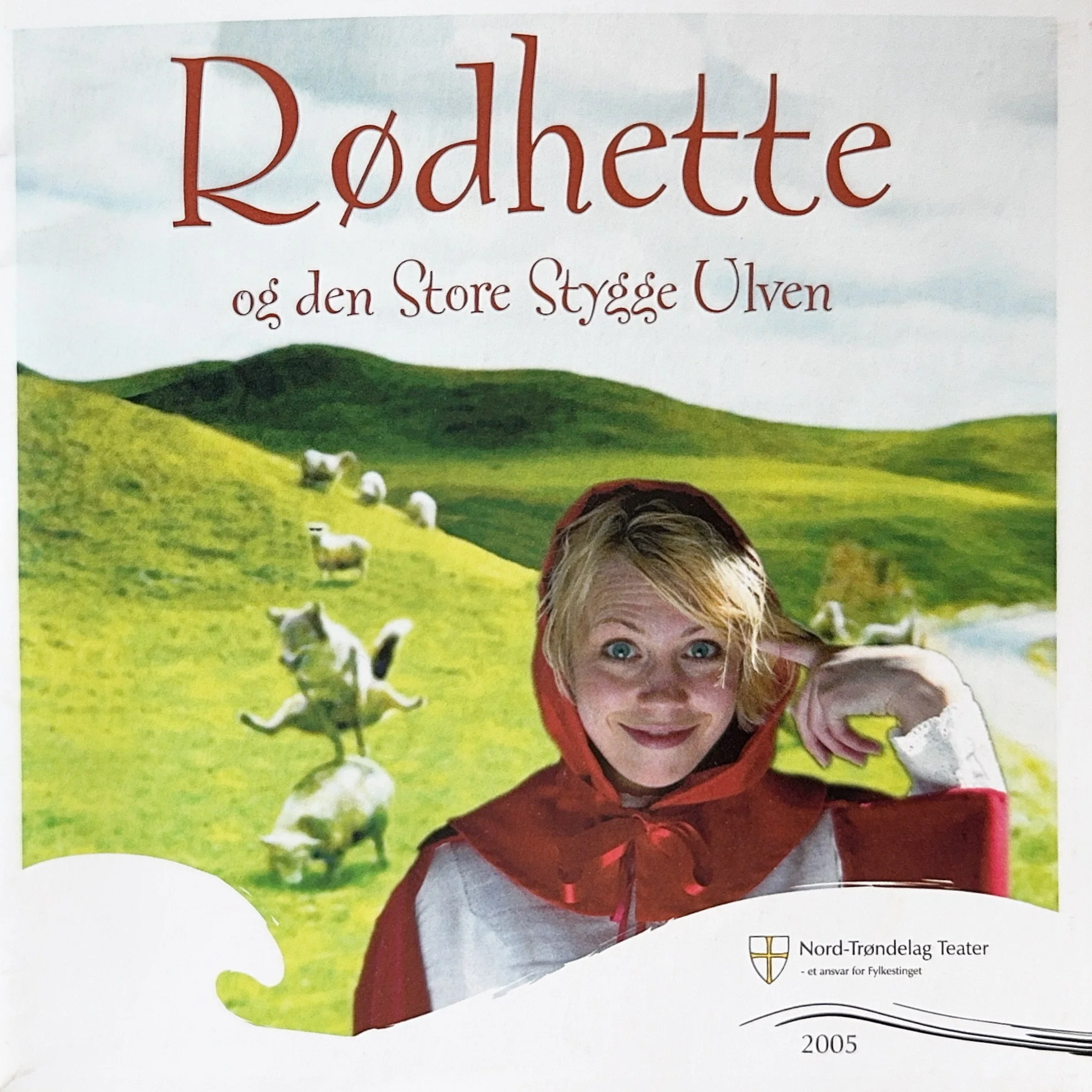 Book cover with a background of green hills and white sheep, featuring a smiling person in a red jacket and grey shirt, with text in Norwegian and a logo for Nord-Trøndelag Teater from 2005.