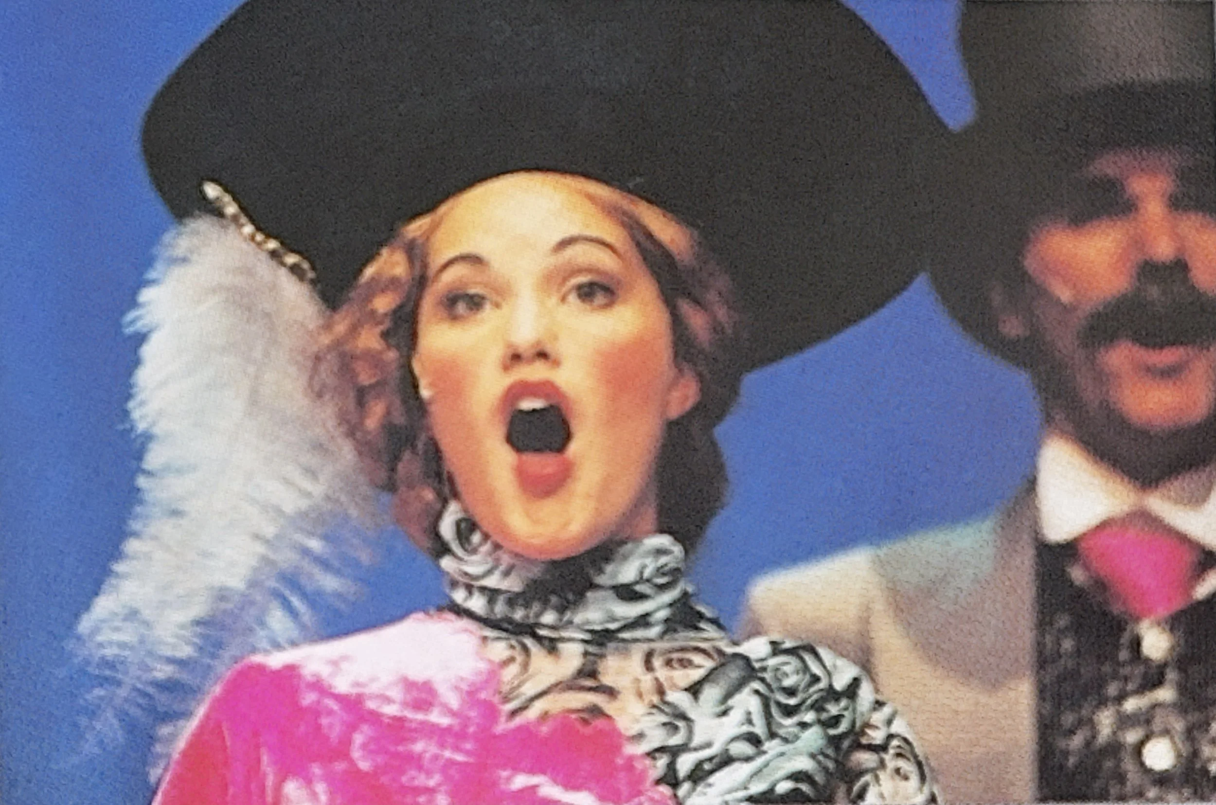 Close-up of a woman wearing a large black hat with a white feather and a pearl headband, with exaggerated makeup and an open mouth.