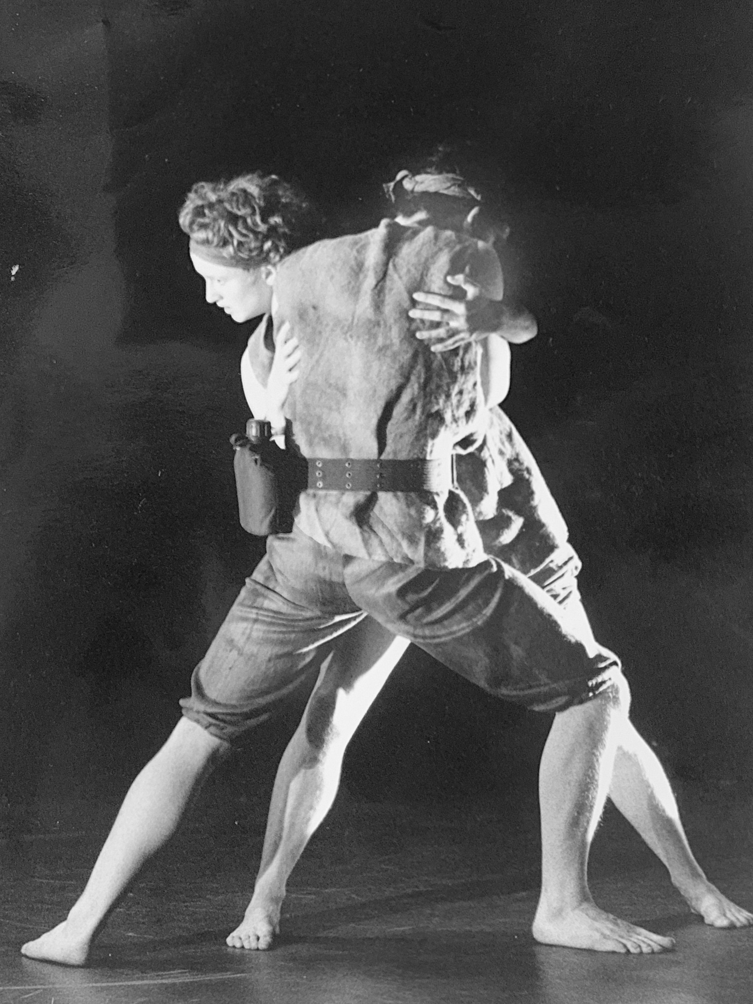 A black and white photo of a man and woman in an intimate embrace, with projections of a person wearing a hat in the background.