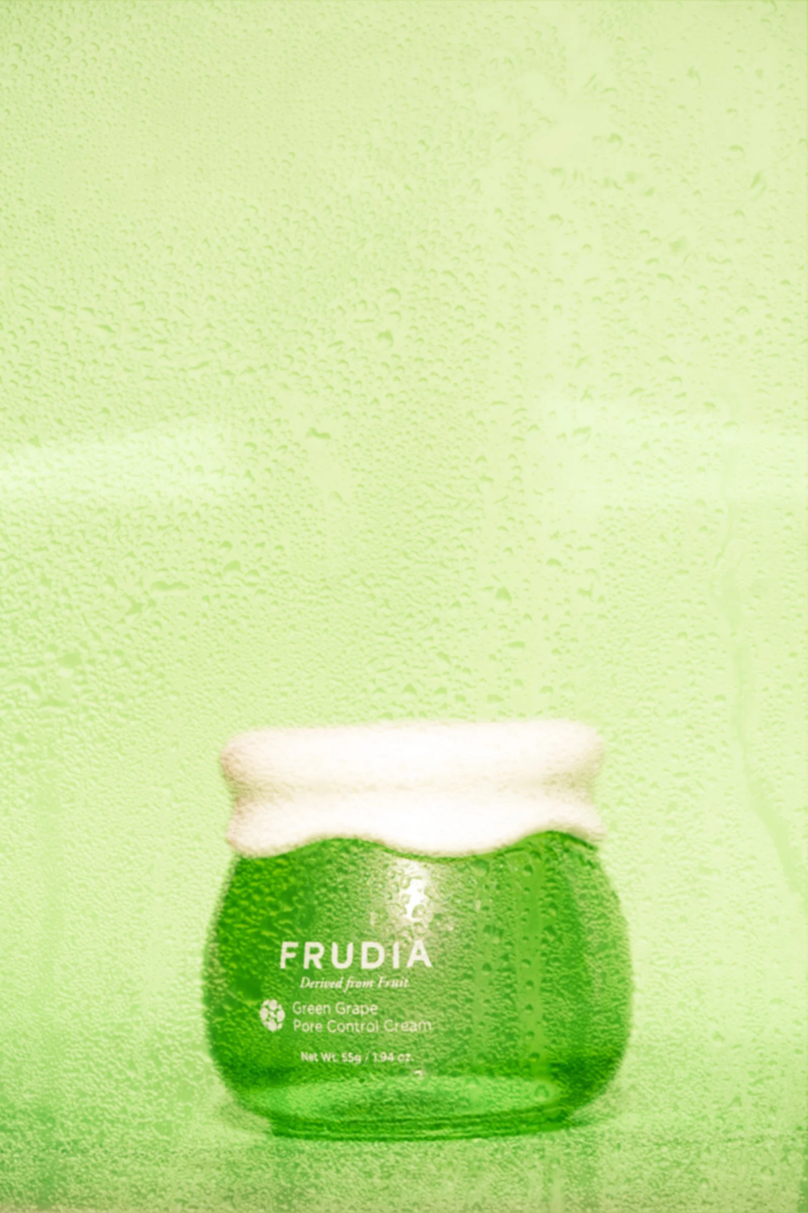 A green bottle of ERUDIA Green Grape Pore Control Cream in front of a green textured background.