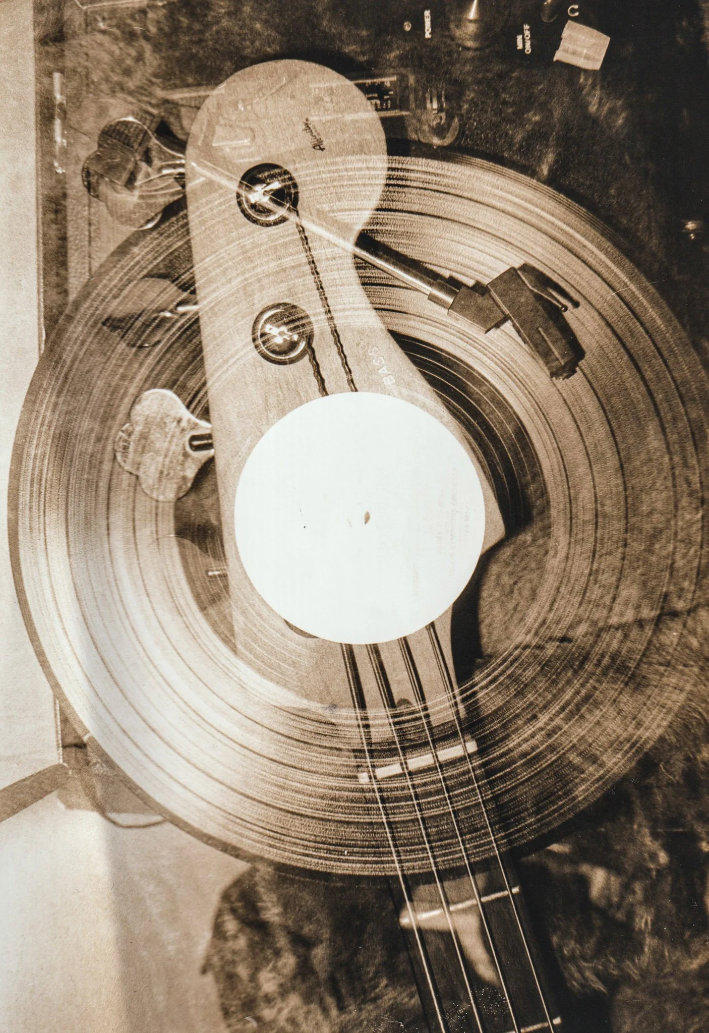 Negative double exposure print. Close-up of a vinyl record on a turntable with an arm and needle playing the record. The background shows various objects including cans, a bottle, and a piece of paper.