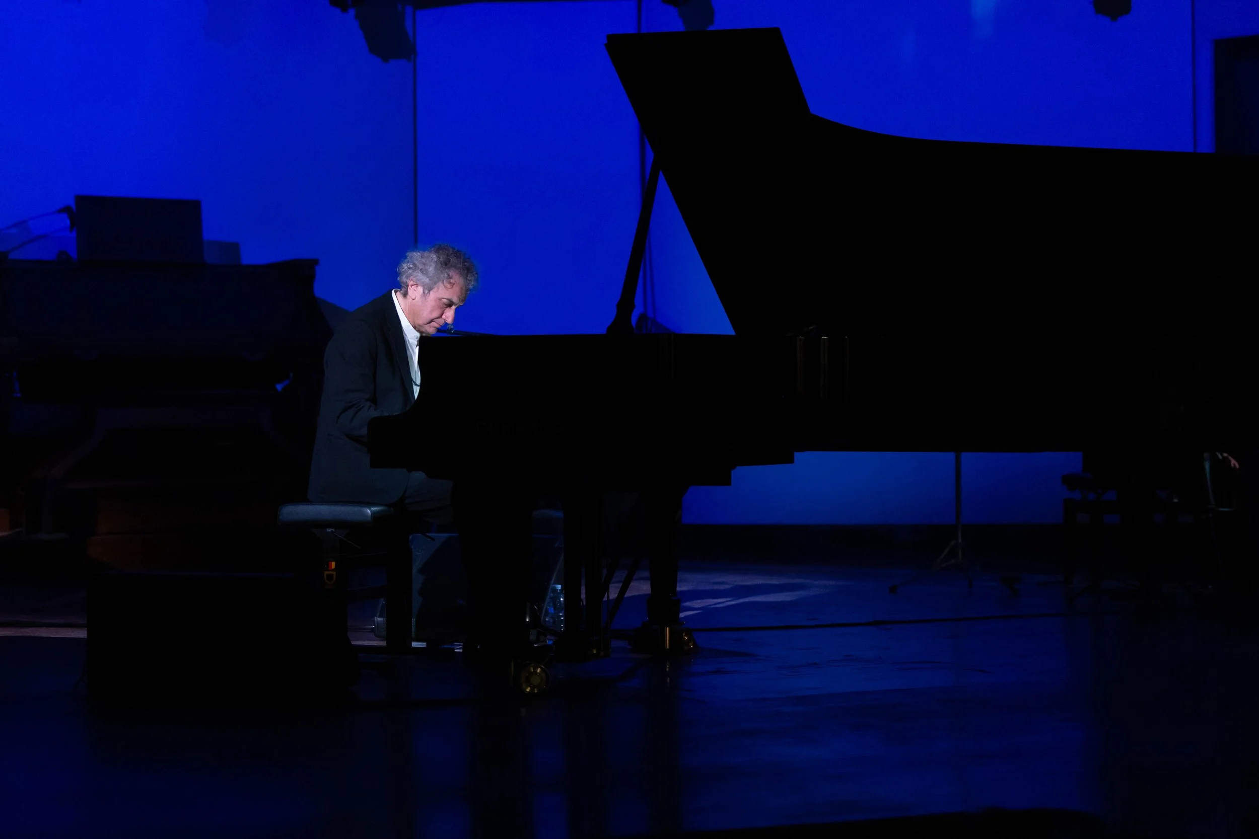 Roberto Cacciapaglia che suona il pianoforte su un palco con luci blu.