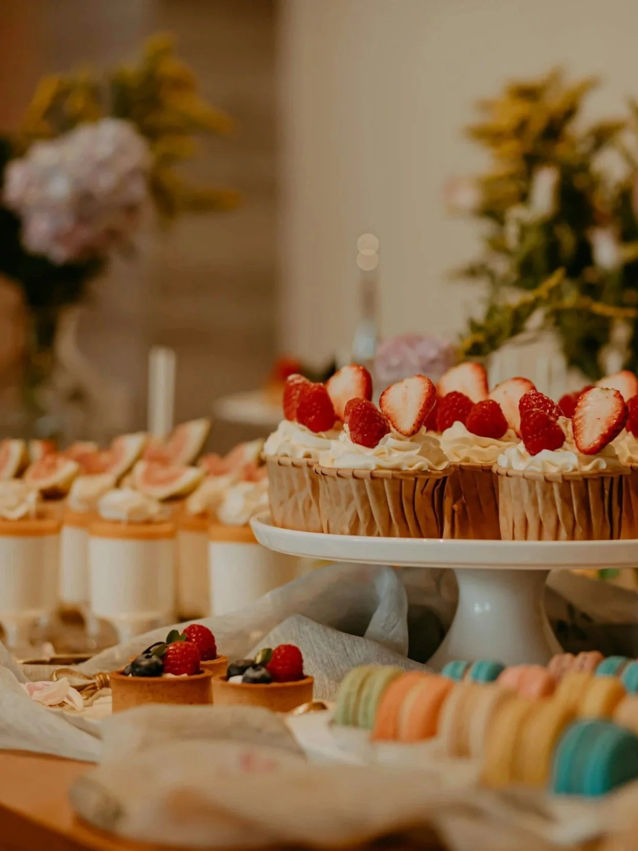 Verschiedene Torten und Minipasteten mit Früchten auf einem Festtisch, mit Blumen im Hintergrund.