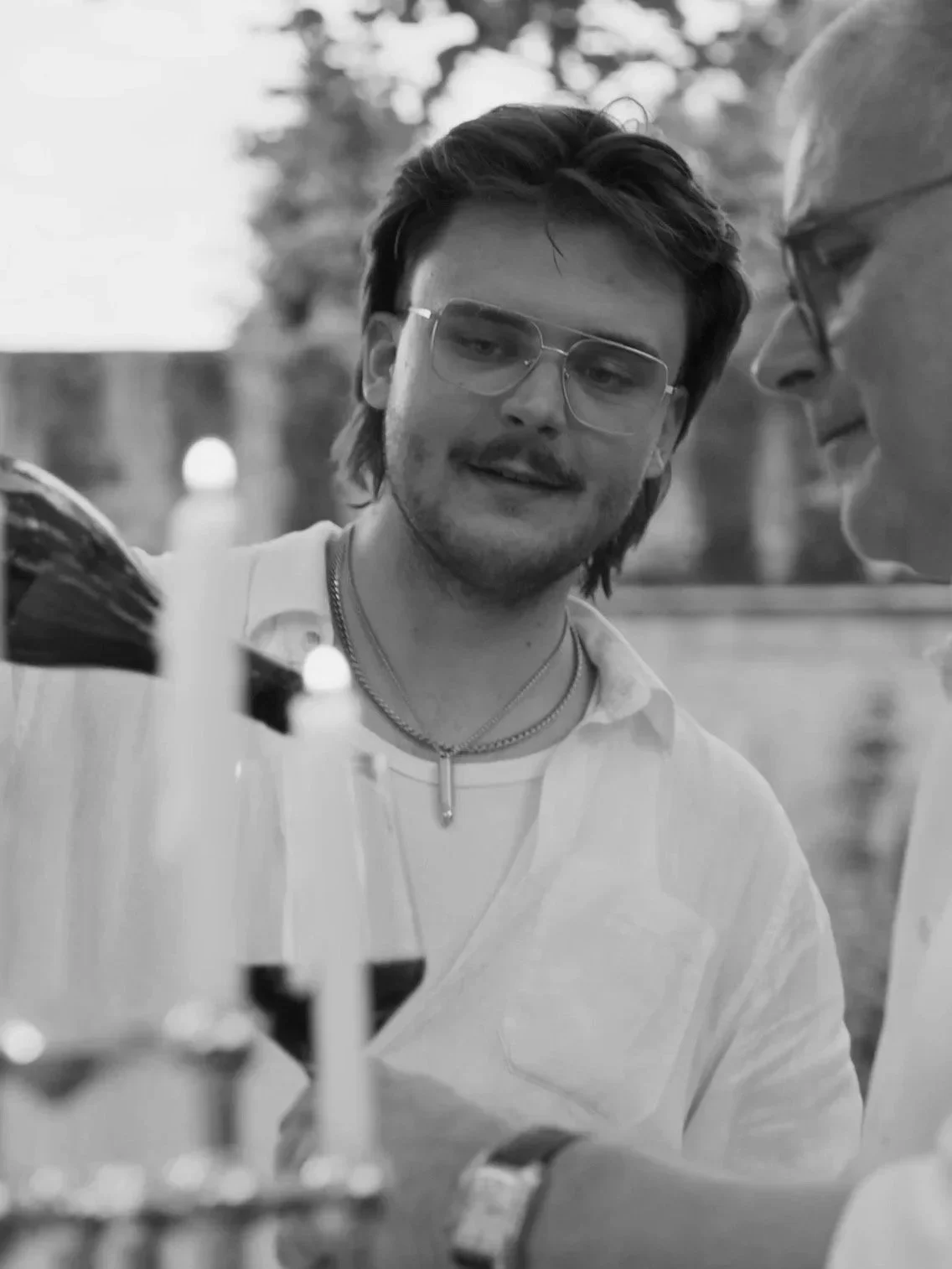 Zwei junge Männer, einer mit Brille, schauen auf ein Experiment mit Fläschchen im Freien, schwarz-weiß.