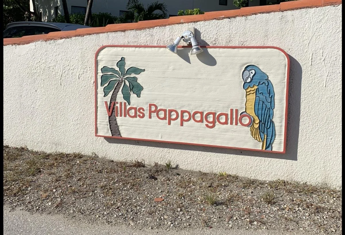 A sign on a white wall reads 'Villas Pappagallo' and features a painted palm tree and a blue and yellow parrot.