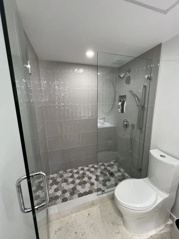 Modern bathroom with a glass-enclosed shower featuring patterned floor tiles and a white toilet next to it.