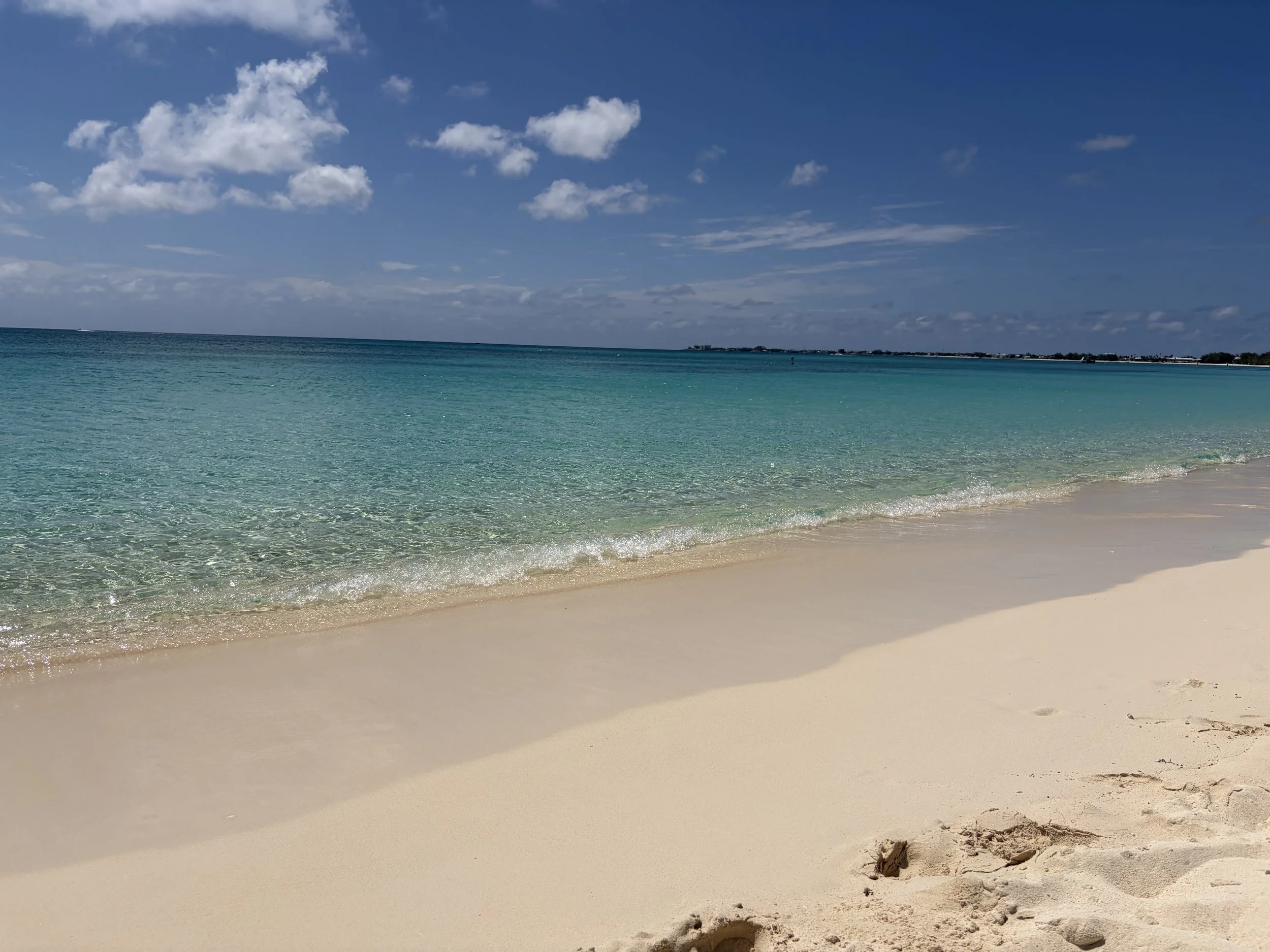 A sandy beach with clear, turquoise water and a bright blue sky with scattered clouds.