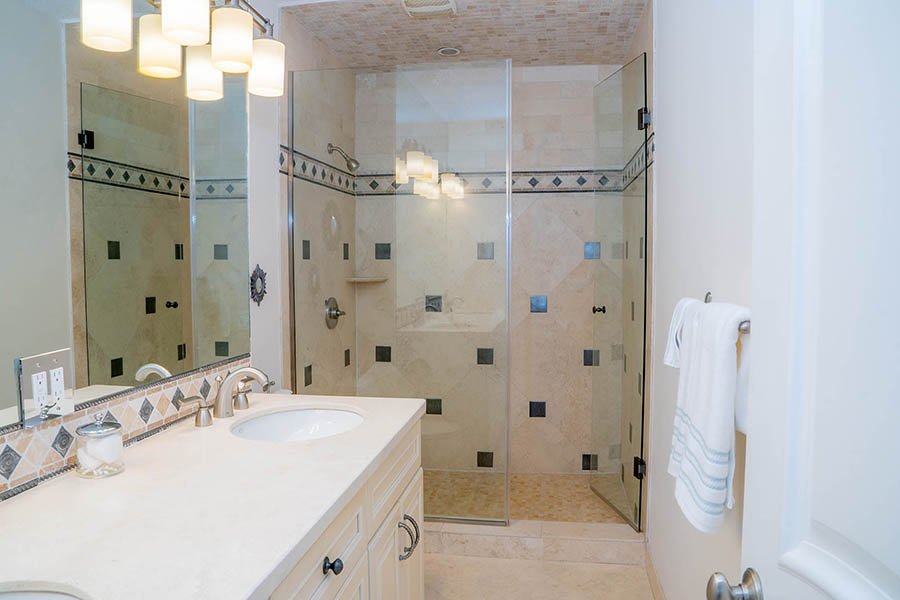 Bathroom with a glass-enclosed shower, a beige vanity with a sink, and a mirror. The shower has decorative tiles and built-in shelves.
