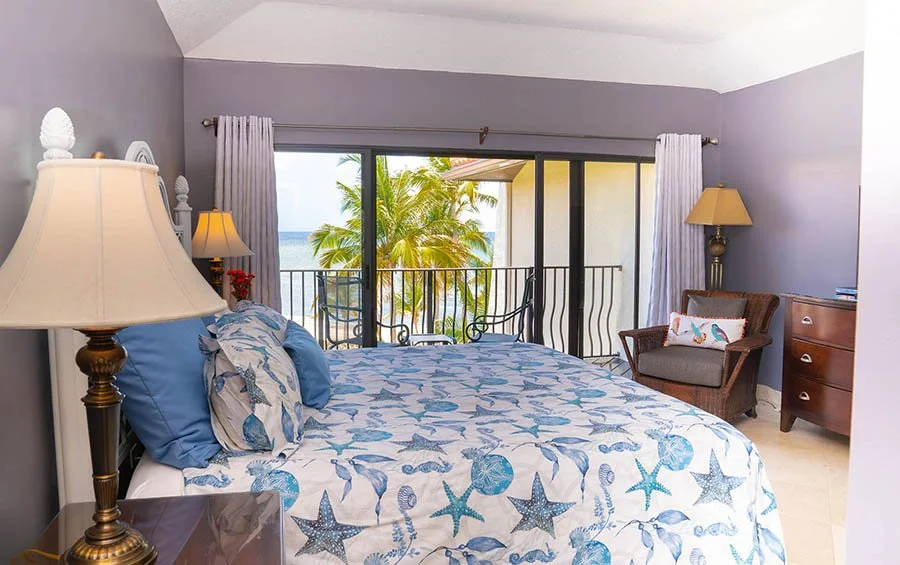 Beach view bedroom with ocean and palm trees visible through sliding glass door, decorated with starfish and seashell themed bedding.
