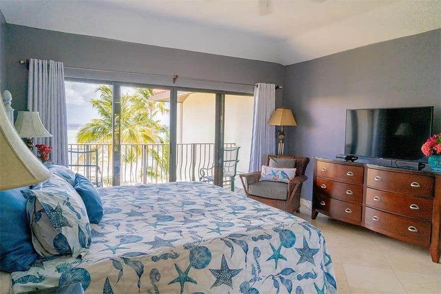 Beachside hotel room with a bed, ocean view balcony, and tropical decor.