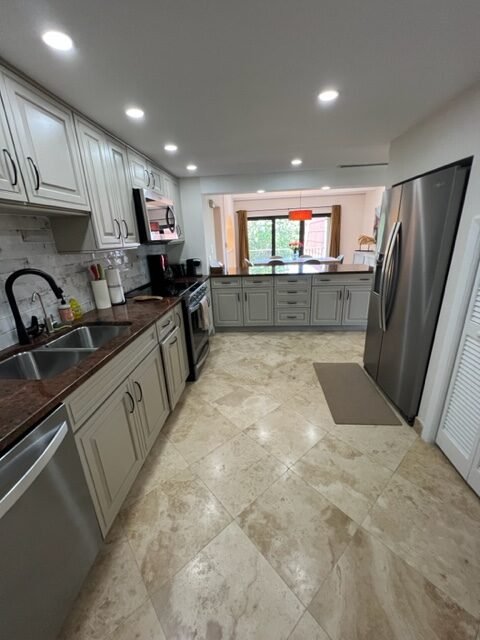 Modern kitchen with beige cabinets, stainless steel appliances, granite countertops, and tile flooring, viewed from the dining area.