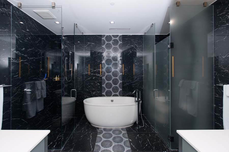 Modern bathroom with black marble walls and floors, a freestanding bathtub, glass shower enclosure, and gray towels.