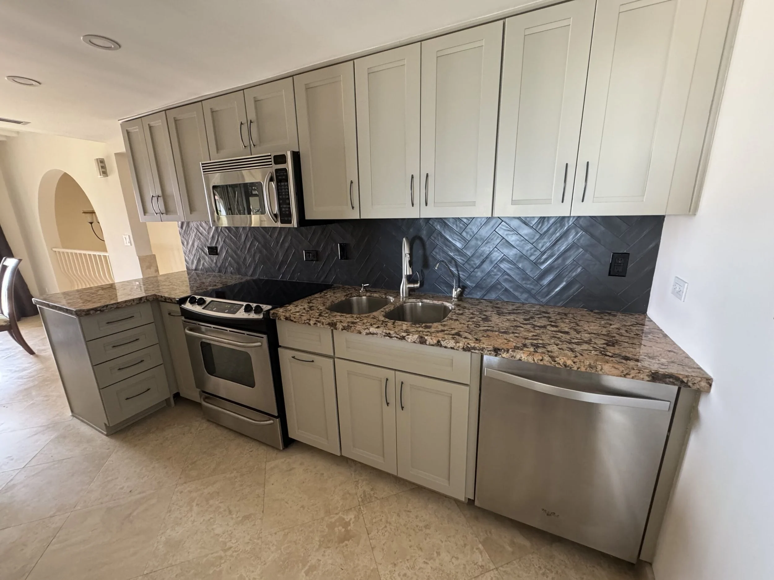 Modern kitchen with white cabinets, stainless steel oven, granite countertop, and dark herringbone backsplash.
