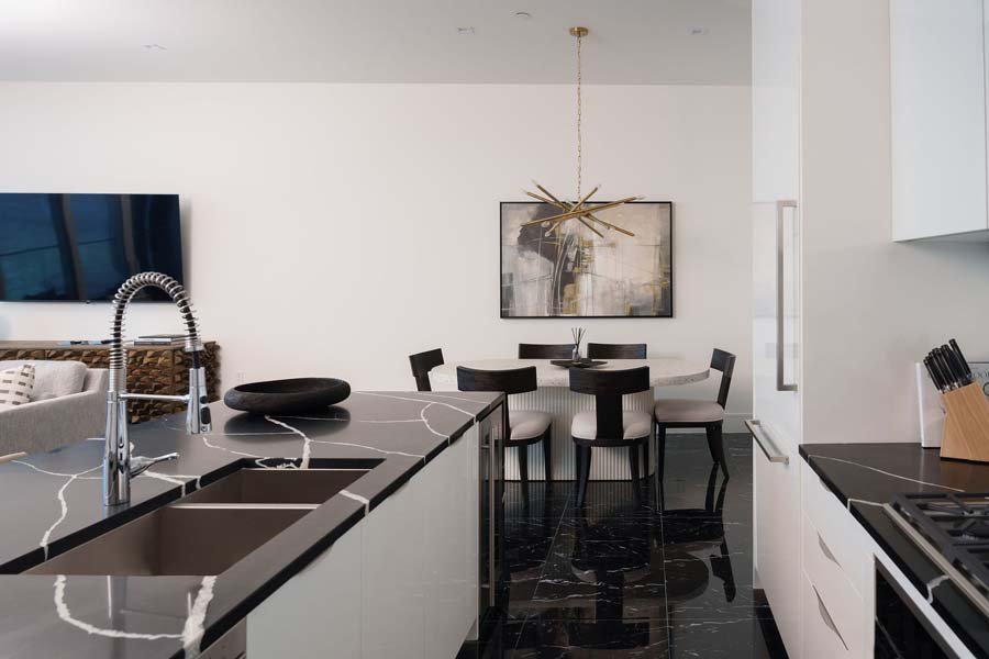 Modern kitchen and dining area with black marble countertops, black and white dining set, and abstract art on the wall.