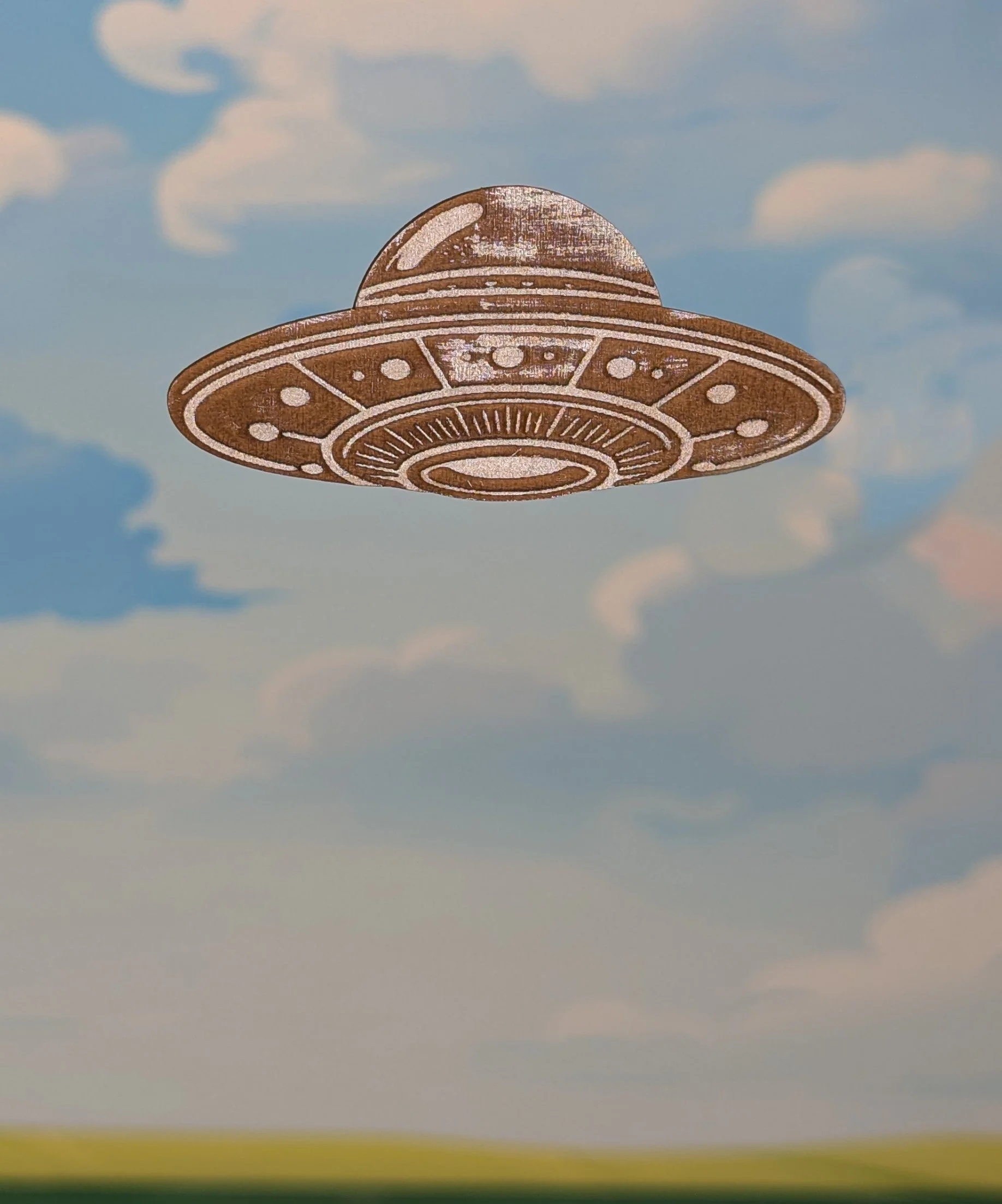 Close-up of a foam toy spaceship with a round dome and detailed patterns, suspended in the sky with clouds in the background.